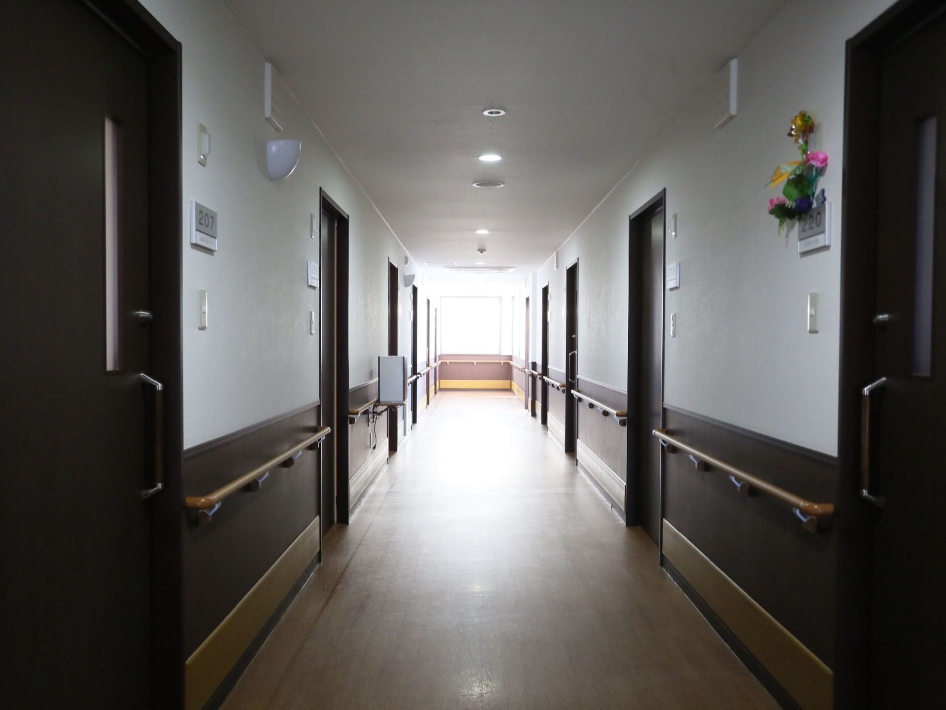 壁が茶系と白のツートンカラーで重厚な趣を醸しだしている。両側に居室が並び、壁に沿って腰高の位置に手すりが設置されている。