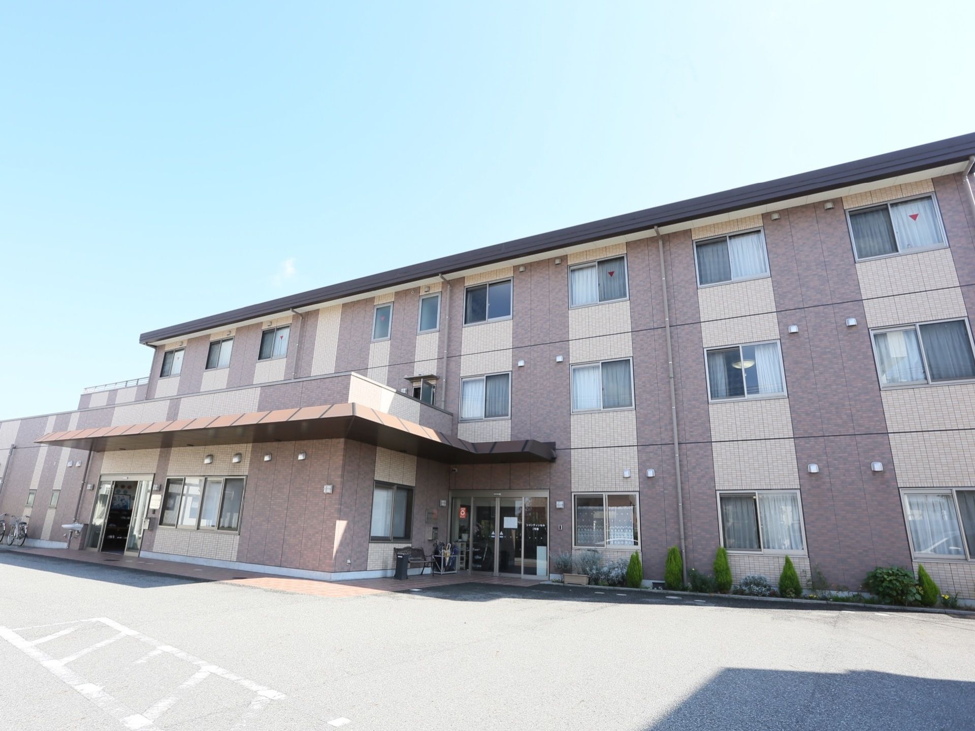 3階建ての建物で、施設前の道路はアスファルトで舗装されている。玄関前には傘立てなどが用意されている。