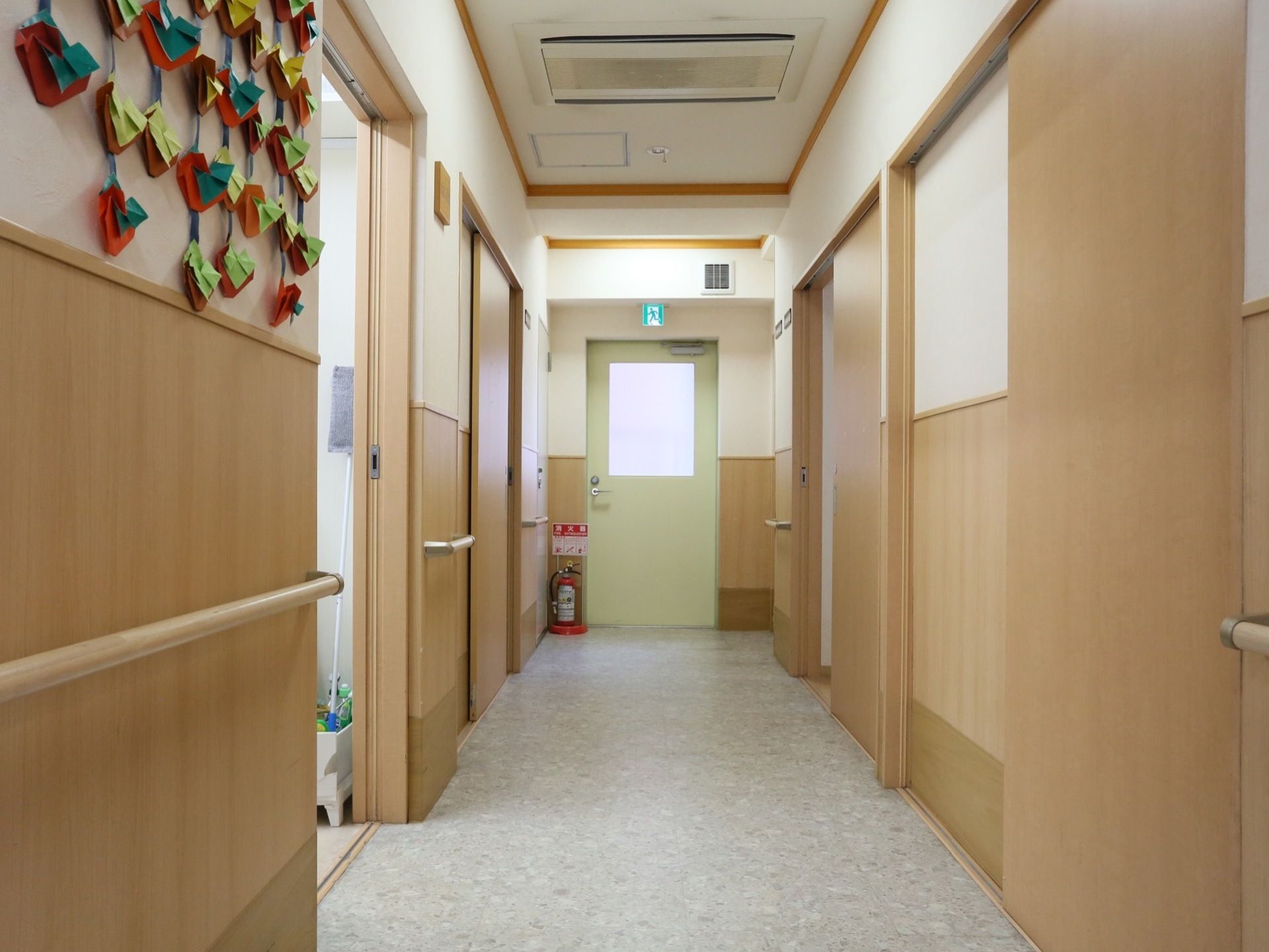 通路の床色はグレーである。白壁に木製の棚板が設置されている。手すりがあり、天井には空調機が備えつけられている。