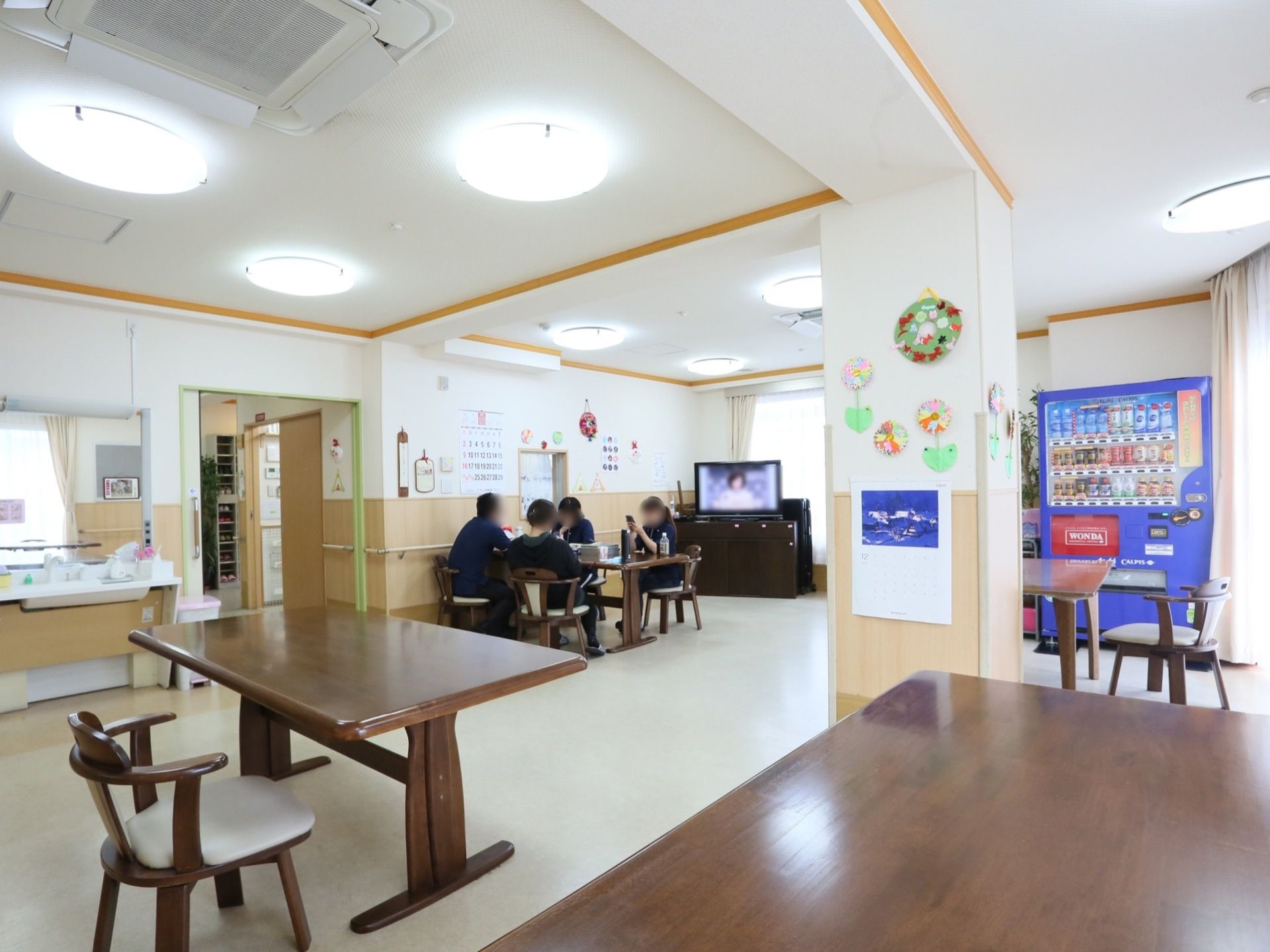 天井に複数の照明が設置されているほか、空調機も完備。濃い茶色のテーブル、椅子複数配置されている。自動販売機もある。