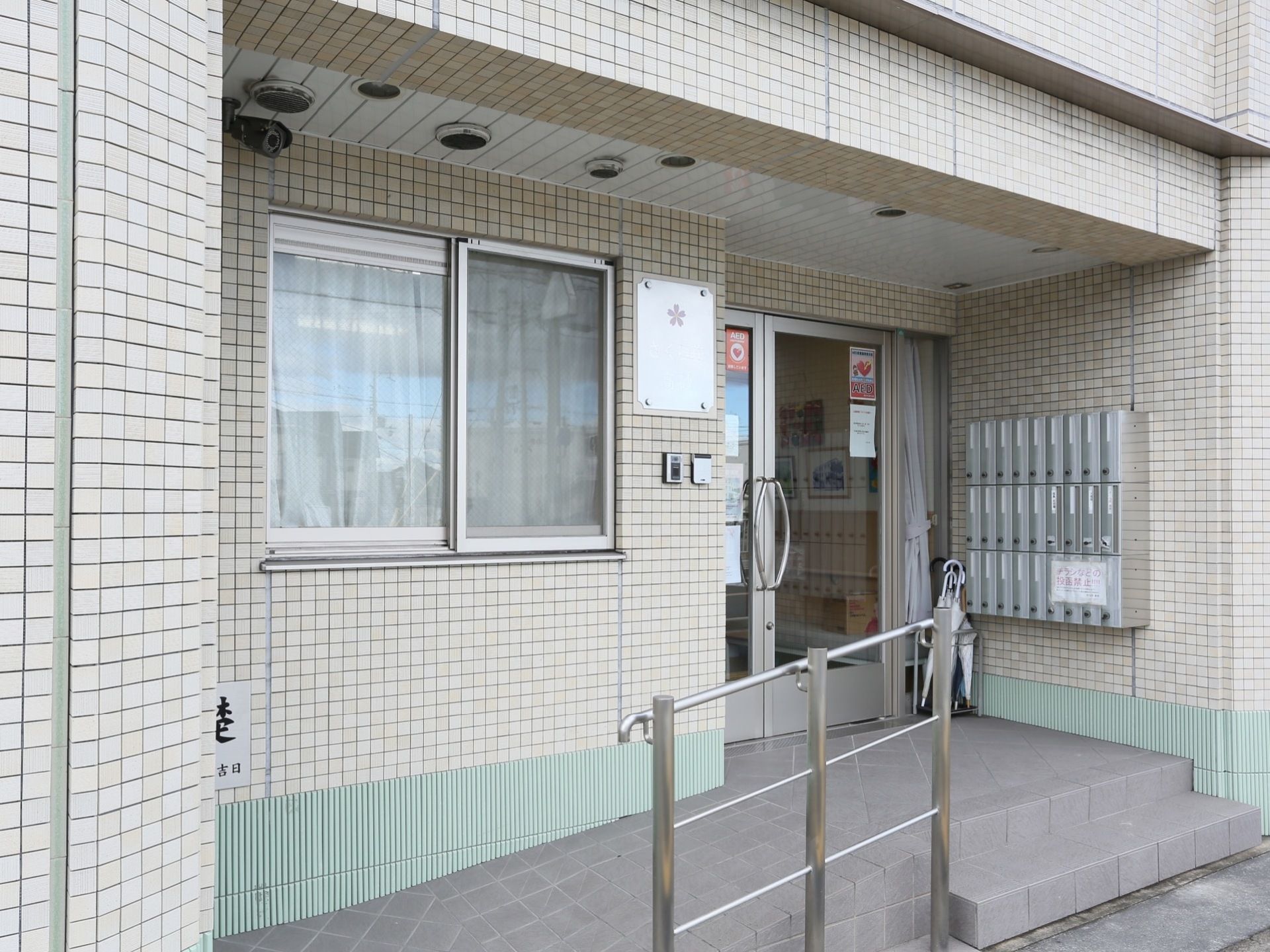 落ち着いた色合いの外壁である。エントランスの床は、グレーのタイルが敷かれている。スロープと階段もある。
