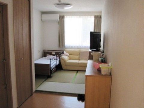 ベッドとソファが置かれた和室と、収納家具が設置されたフローリングがある居室