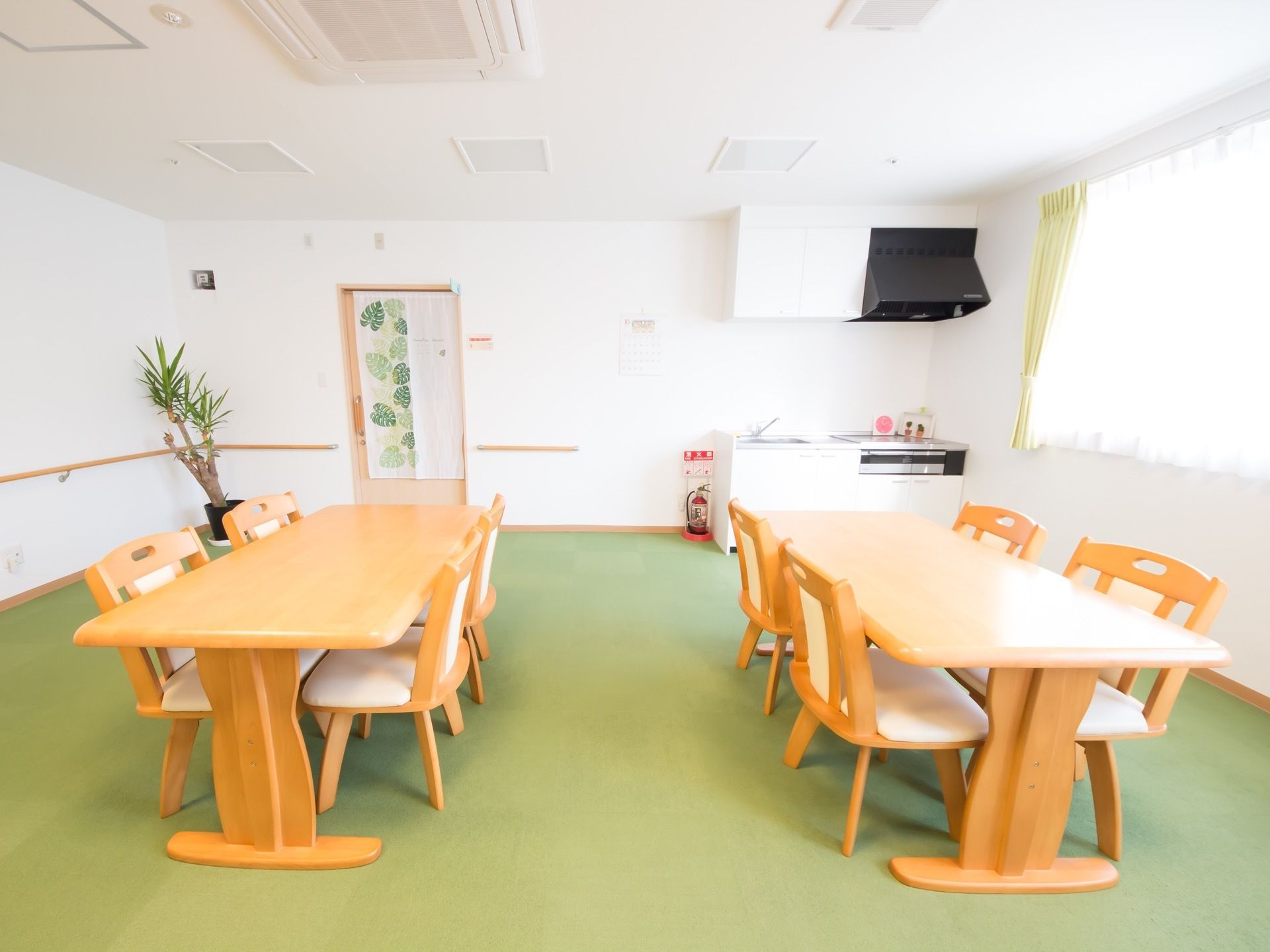 木製のテーブルが二つ置かれている共有スペース。部屋の隅にはキッチンがあり、万一に備えた消火器が設置されている。