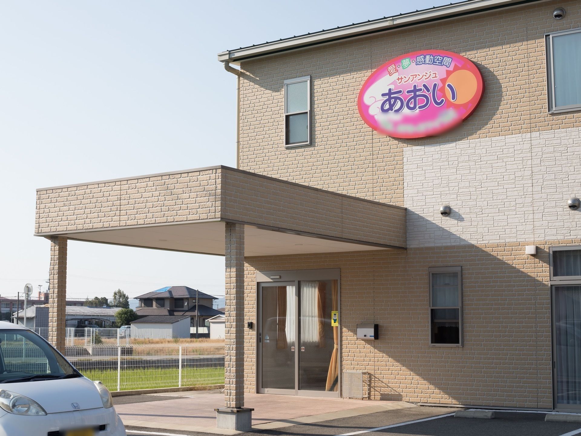 玄関前に車寄せがあり、正面の壁に大きな看板が付いている２階建ての建物