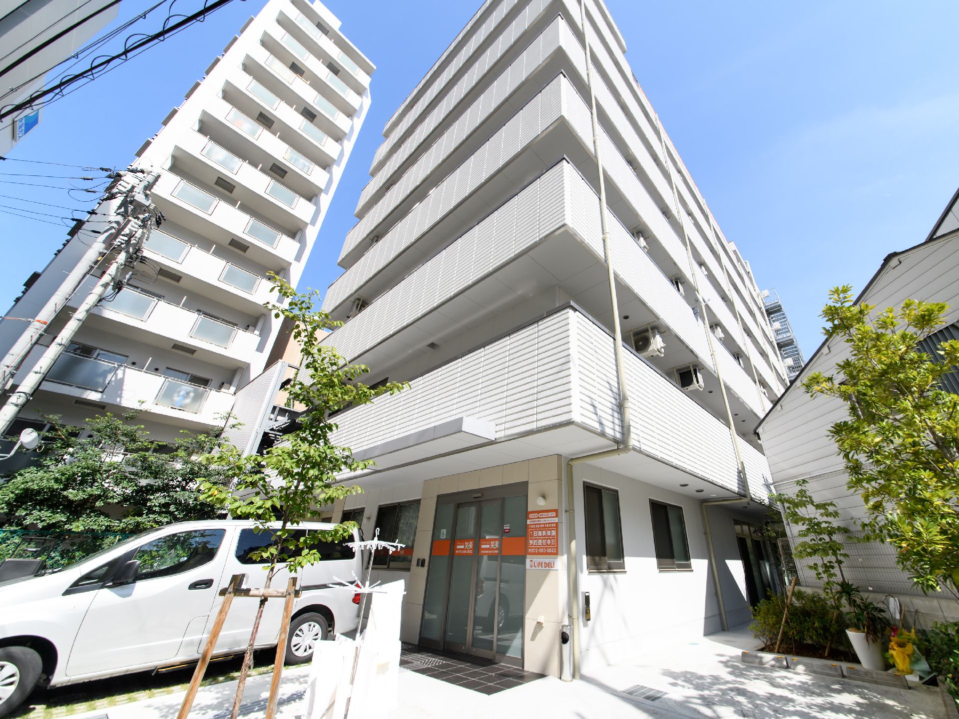 陽当たりの良い場所に立地している7階建ての私設の外観。建物の前には木が植えられ、駐車スペースが設けられている。