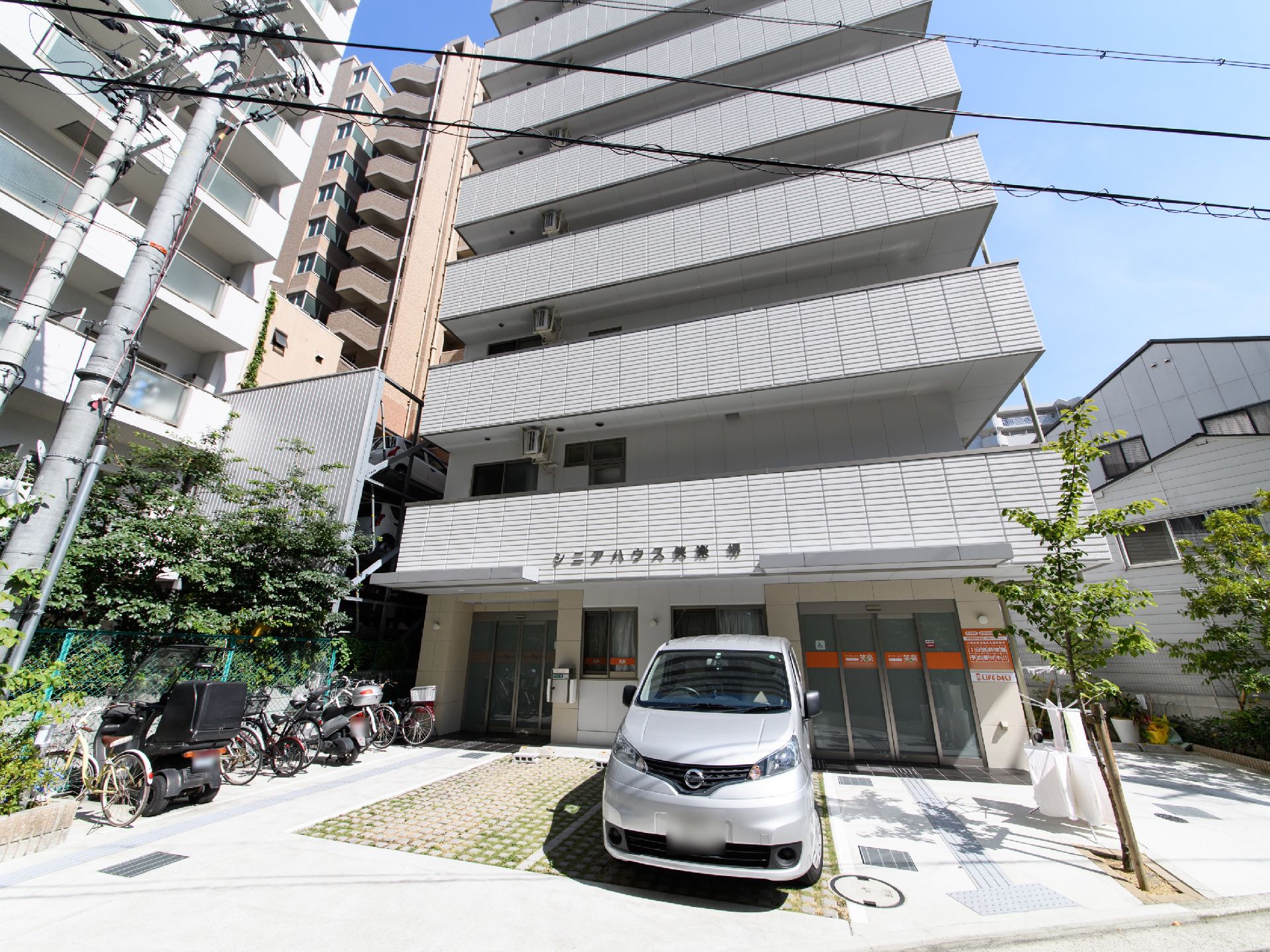 マンションや戸建てが建ち並ぶ住宅街に建てられている7階建ての施設の外観。建物の前には駐車スペースがある。
