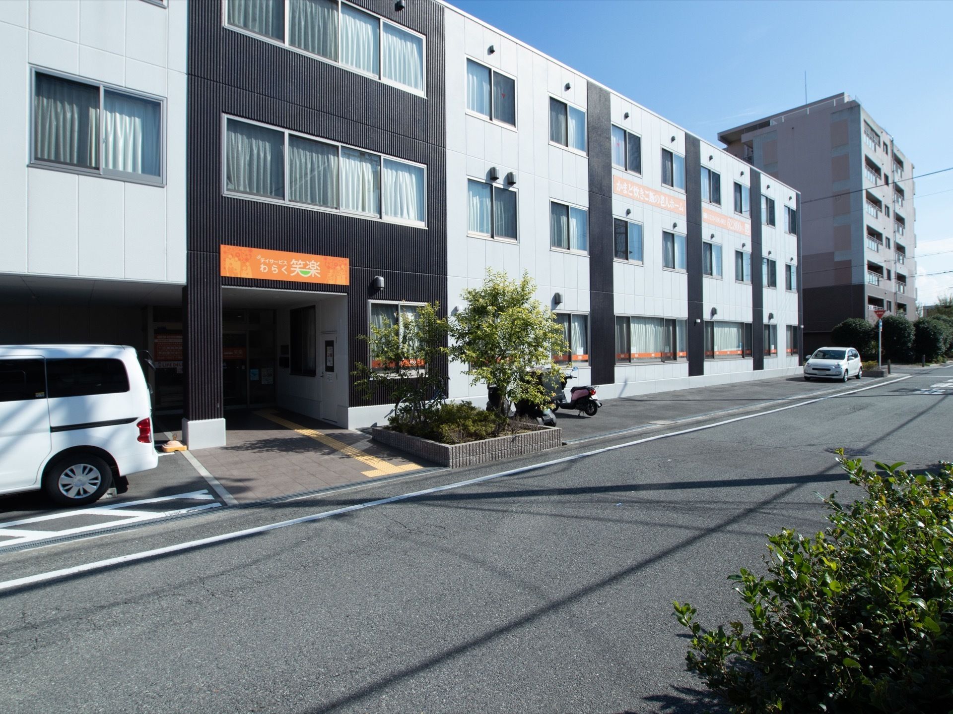 施設は３階建てで、白色と黒色で統一された外壁となっている。玄関前の一角には、木や植物が植えられている。