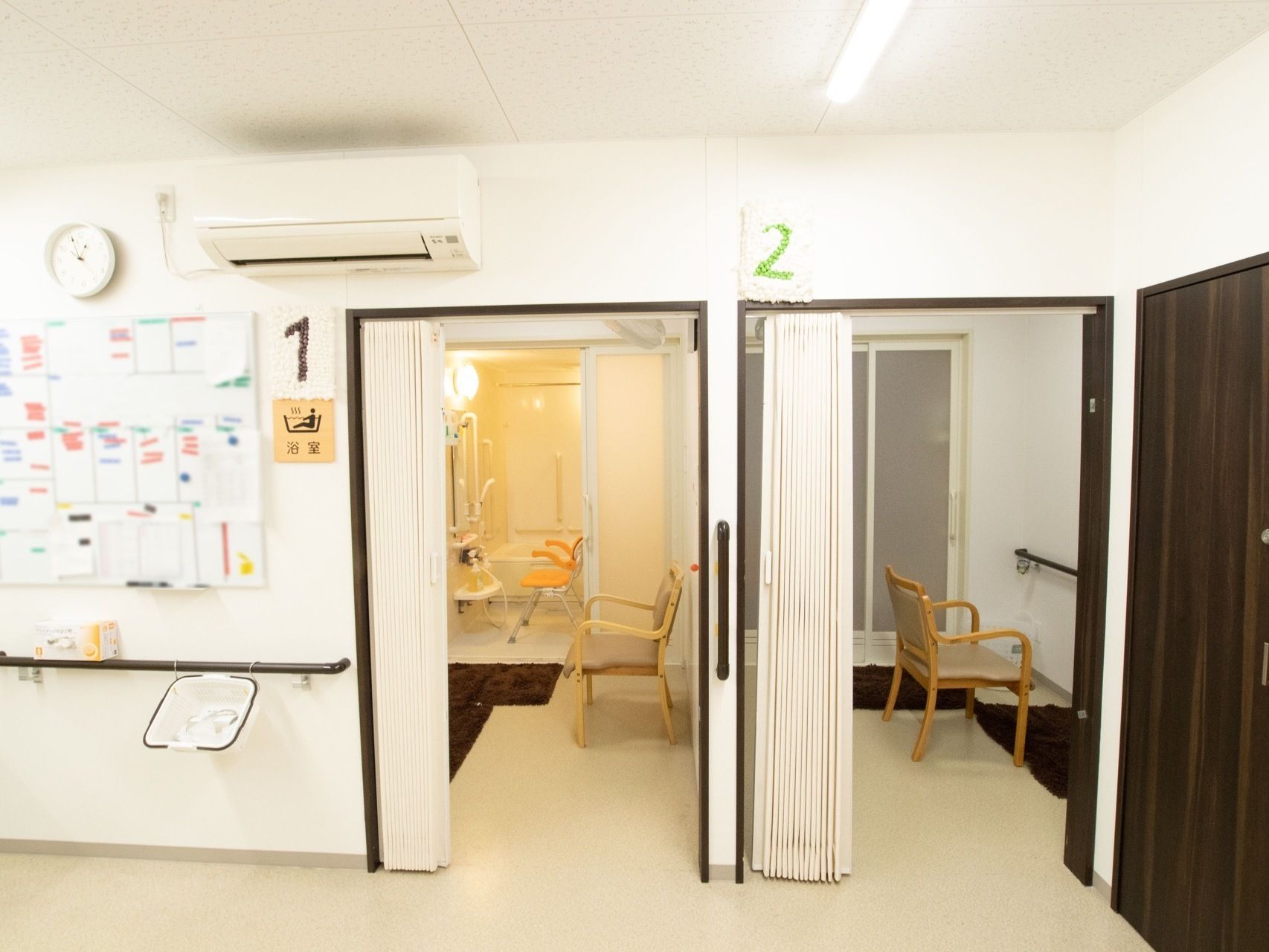 横並びに２つの浴室が完備されている。脱衣所に椅子が置かれている。入口近くの壁には、大きなエアコンが設置されている。