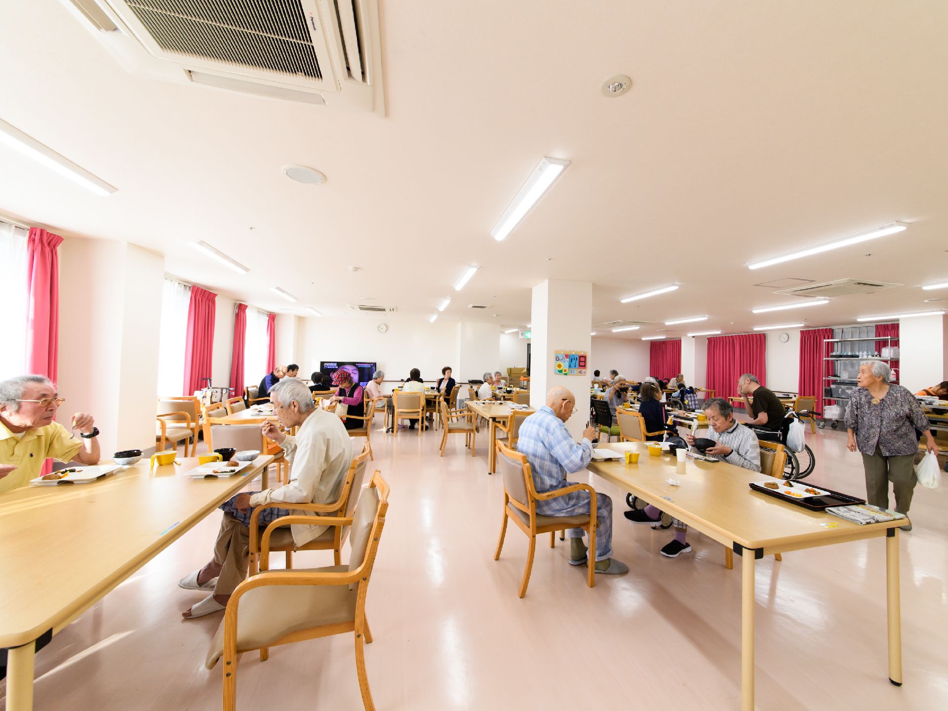 スペースにゆとりをもって、テーブルが配置されている食堂。入居者様たちが大きなテーブルでゆったりと食事をしている。