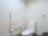 温水洗浄便座を設置したトイレで、壁にはL字型の手すりが取りつけられている。手すりの上に非常ボタンがある。