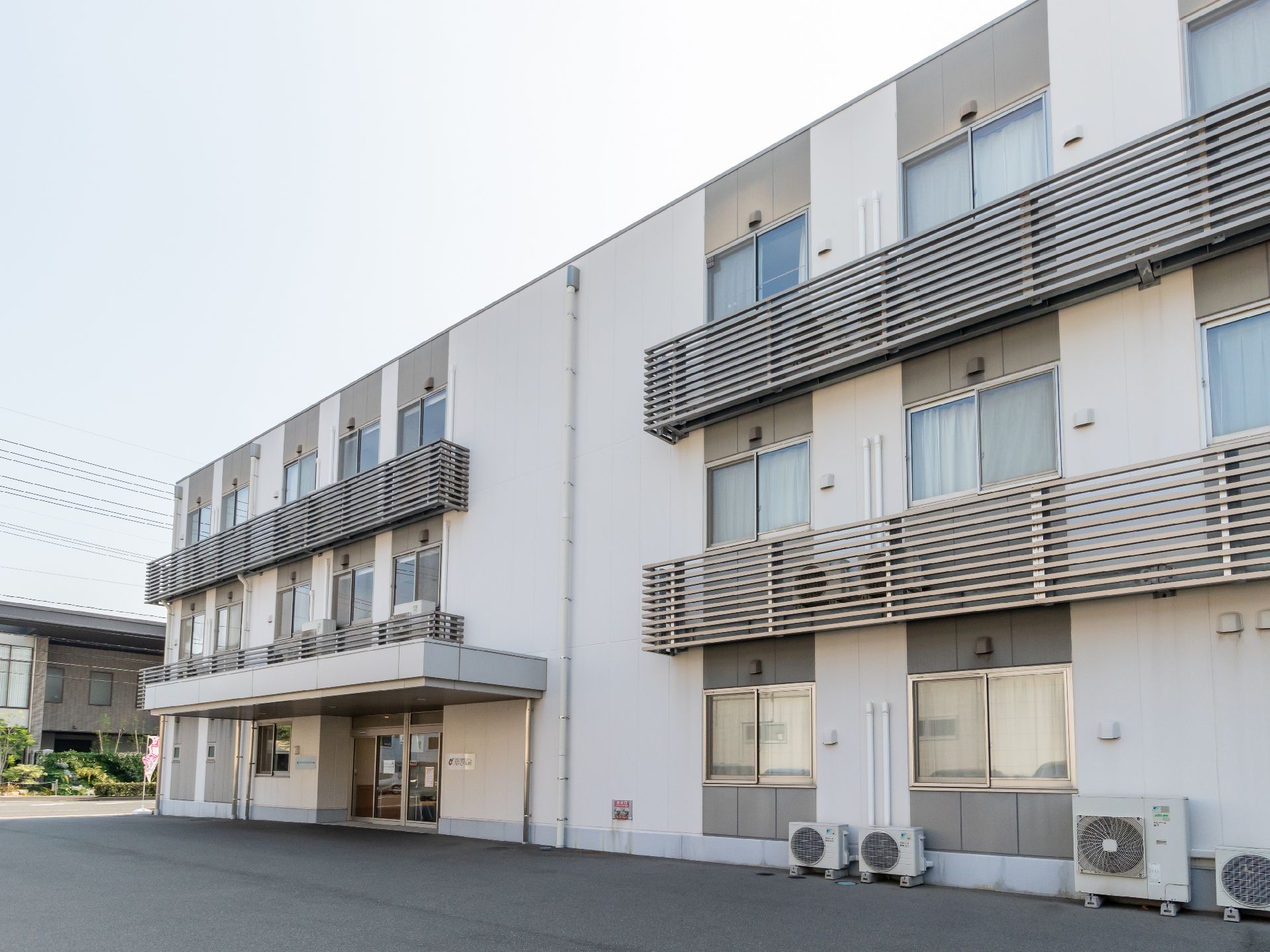 アスファルトに隣接して立地している３階建てで白い外観の建物