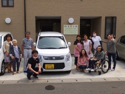 建物の前の駐車場で集合して笑顔を浮かべる入居者様とスタッフ