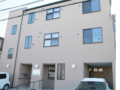 前に駐車場とスロープが設置されている、3階建ての建物