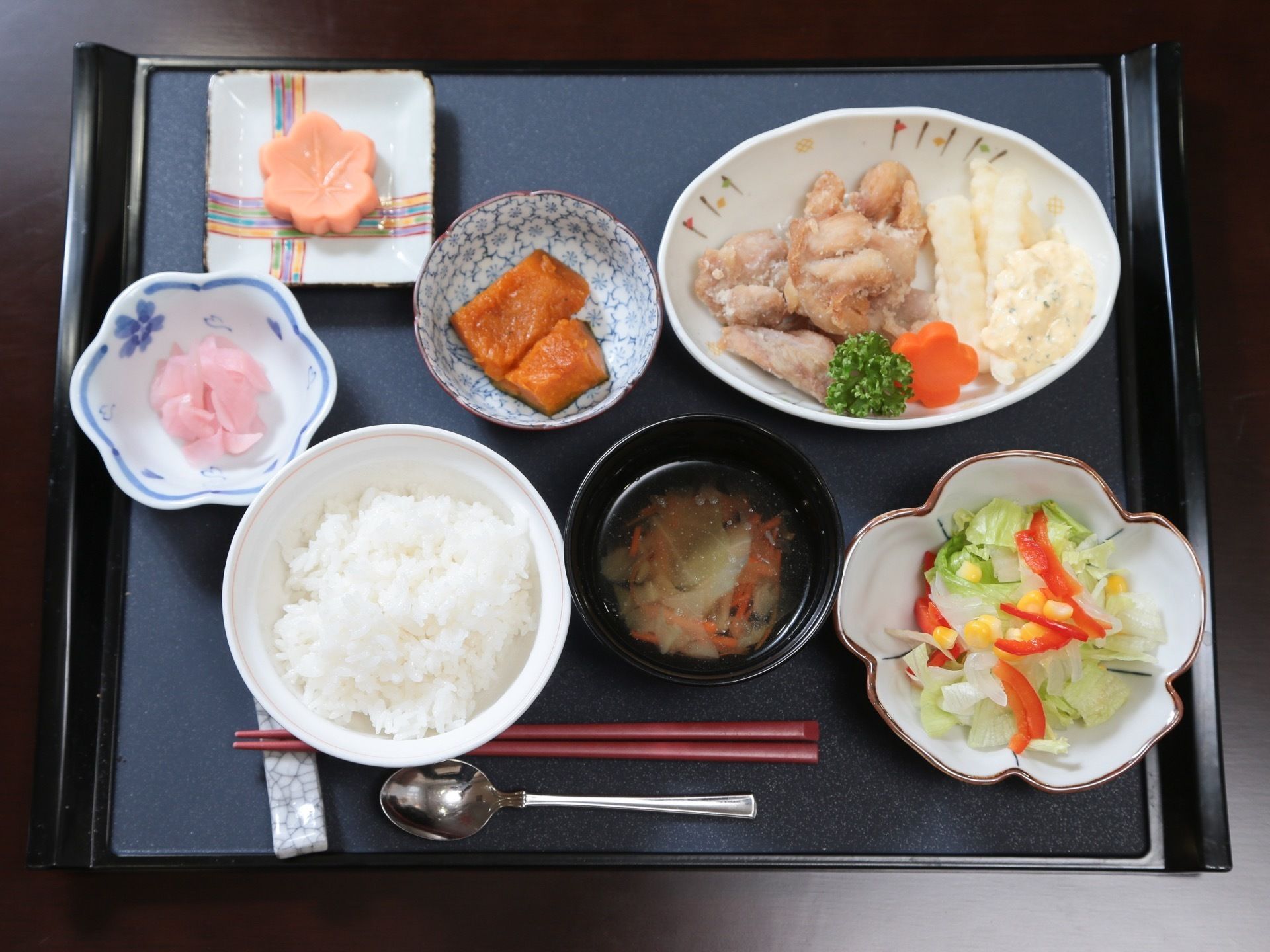 黒いトレーの上に、ご飯と味噌汁、キャベツのサラダ、から揚げとフライドポテト、カボチャ、漬物、もみじ形の和菓子などが並んでいる。