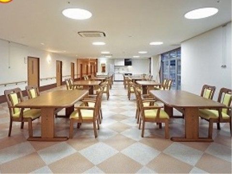 「ケアホーム ディア・レスト岩国」の食堂・デイルーム。チェック柄の床に、4人一テーブルになっている。