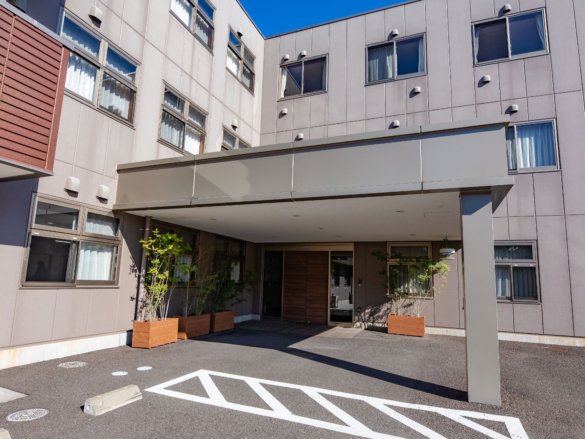 大きな屋根がついている。観葉植物が置かれている。グレーを基調とした落ち着きのある佇まいである。駐車場が隣接している。