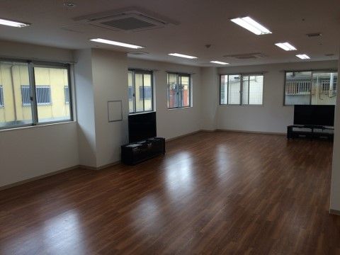 大型テレビが置かれ、窓が多く並んでいる、濃い色のフローリングの部屋