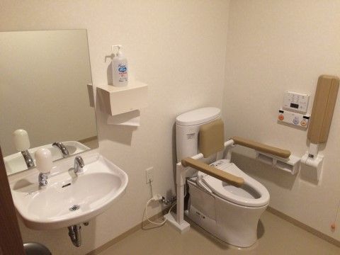 便座の両脇に手すりが付いており、前には折り畳み式の手すりがある。壁には操作パネルや、呼び出しボタンが設置されている。