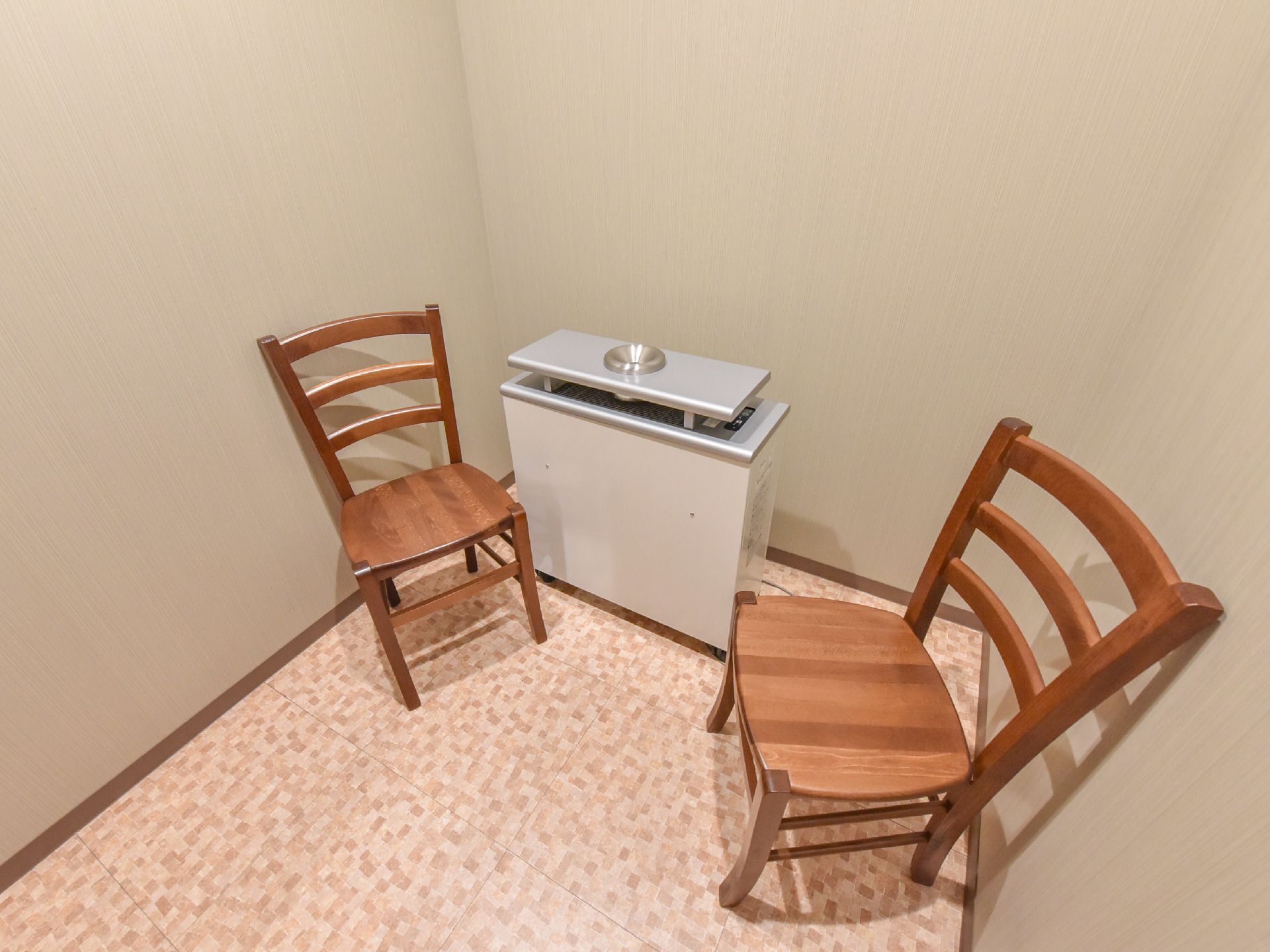 ベージュ色の壁で囲まれた喫煙コーナーには、集塵脱臭機が備え付けられている。四角い機械の両側に、茶色のイスがある。