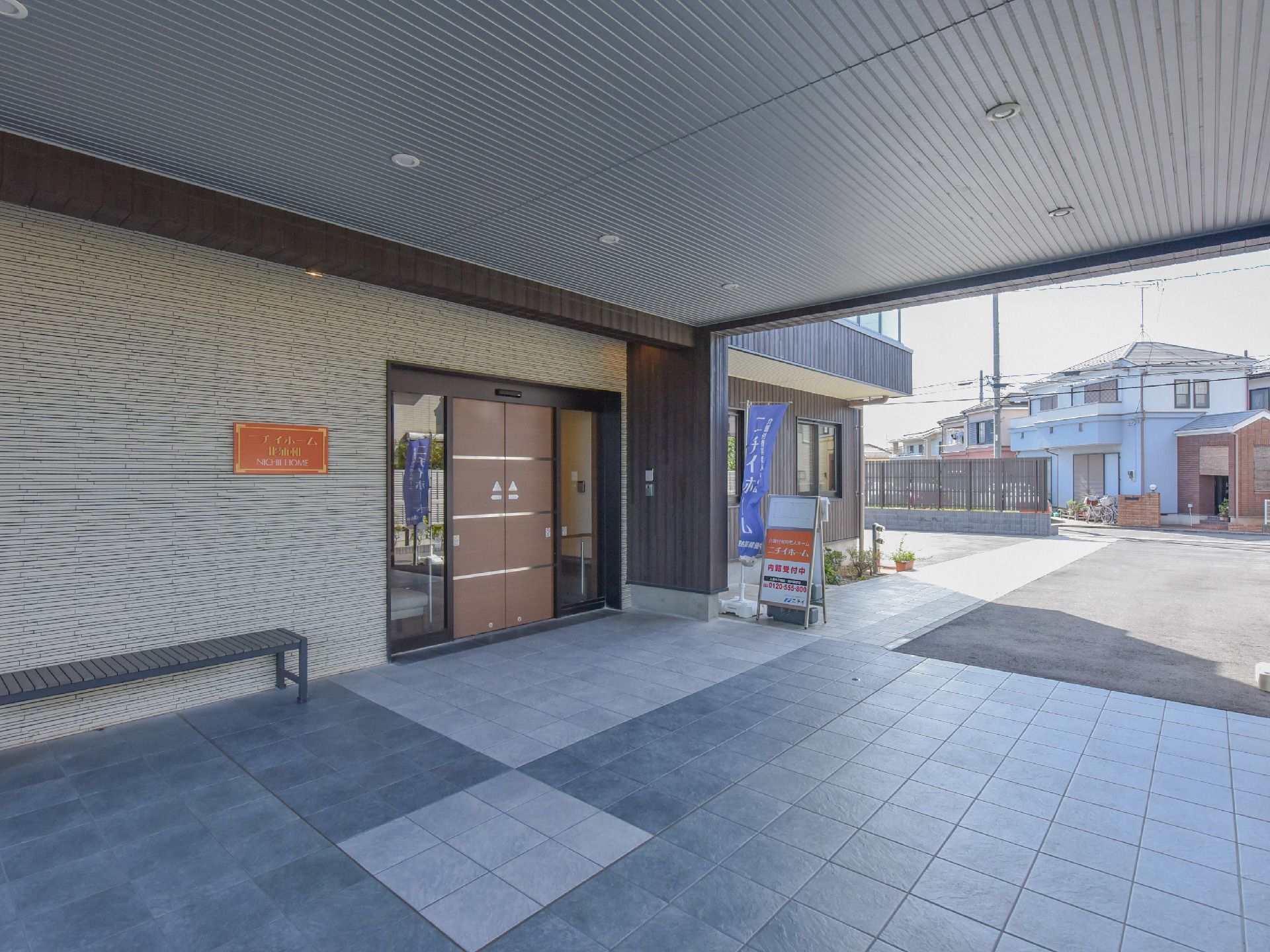 自動ドア前方の床は、薄いグレーと濃いグレーの2色のタイルが組み合わされたデザインとなっている。青いのぼりが立てられている。