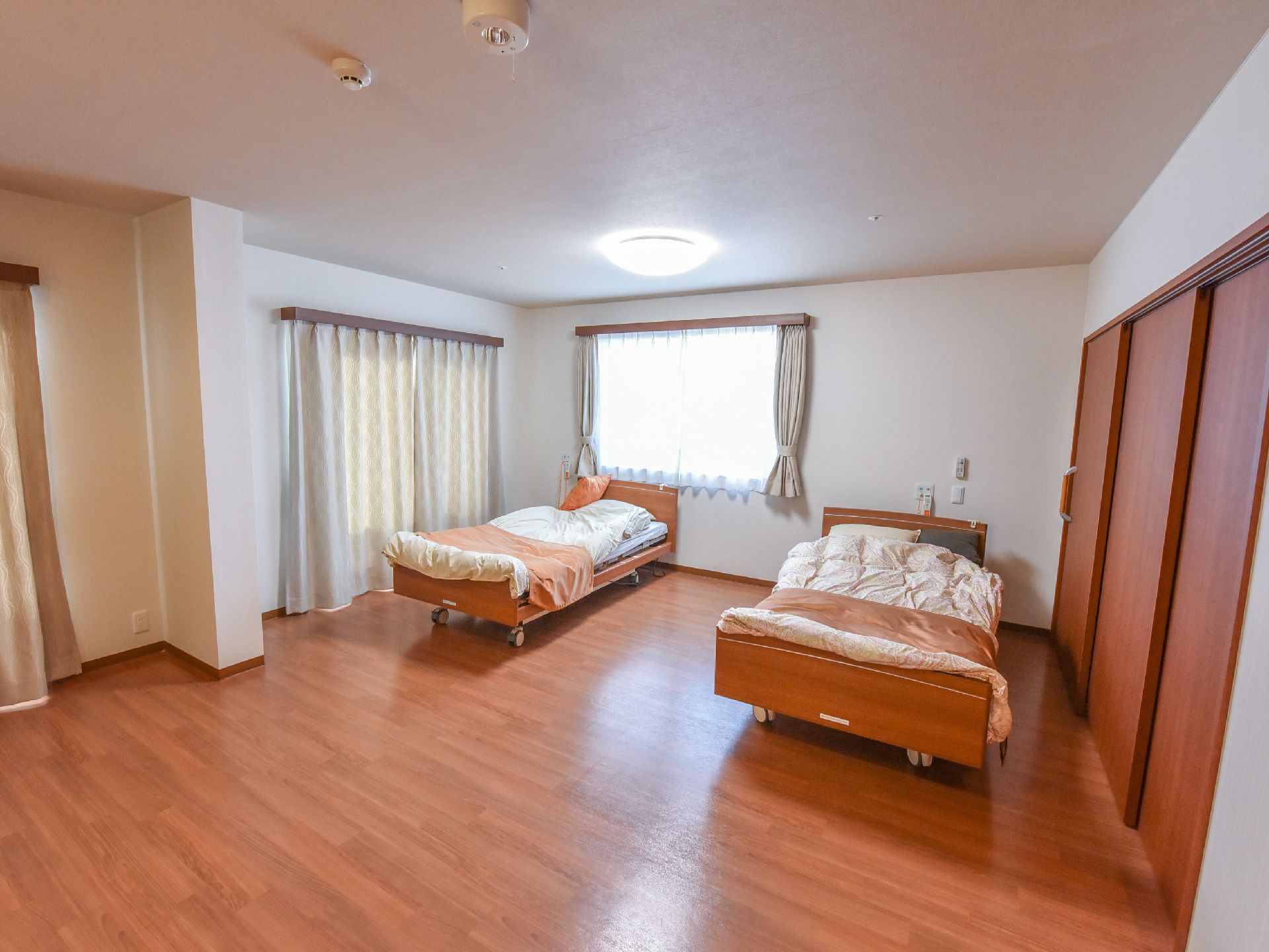 夫婦室の2面の壁には、大きな掃き出し窓と腰高窓が取り付けられている。それぞれの窓には、ベージュ色のカーテンが付いている。