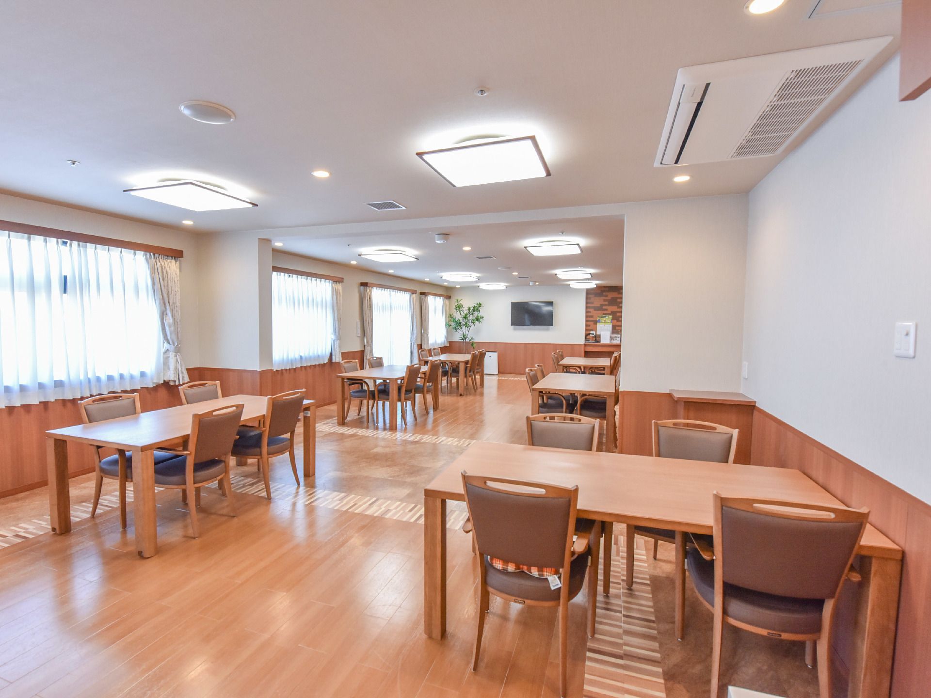 4つ以上ある大きな窓からは日光が良く入るようになっている。部屋には茶色いテーブルと椅子が並べられている。