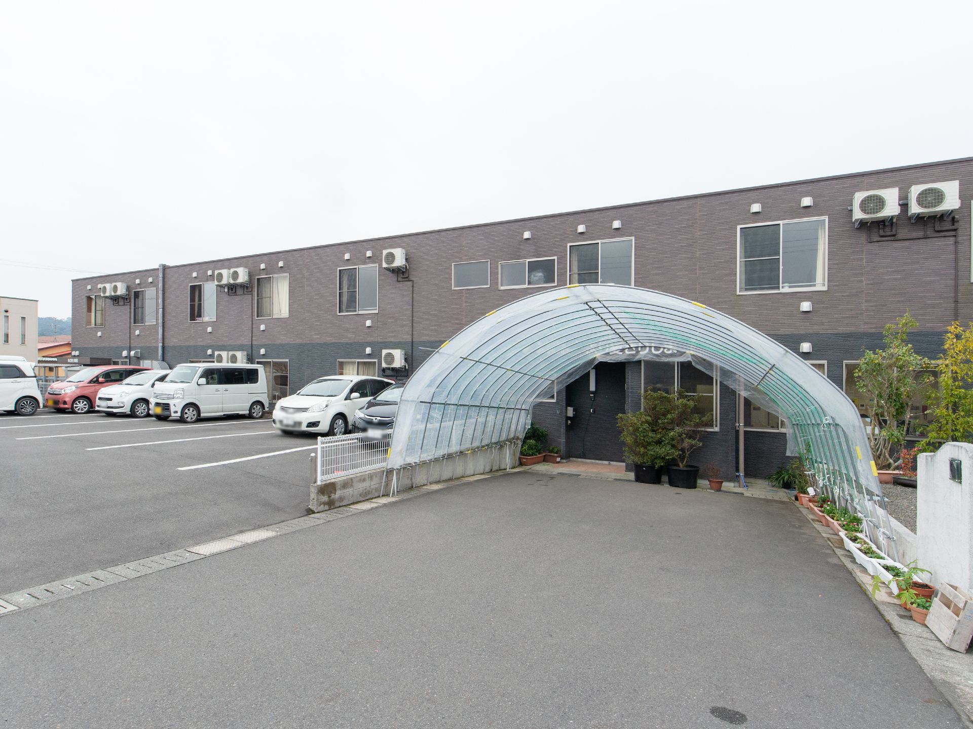 ２階建ての大きなホーム。施設目の前にはビニールハウスが設置されており、複数のプランターが並べられている。