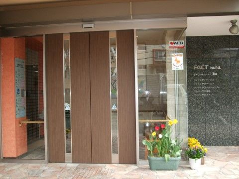入口は自動ドアで、外には点字ブロック、中には手すりが設置されている。花の植えられた植木鉢が飾られている。