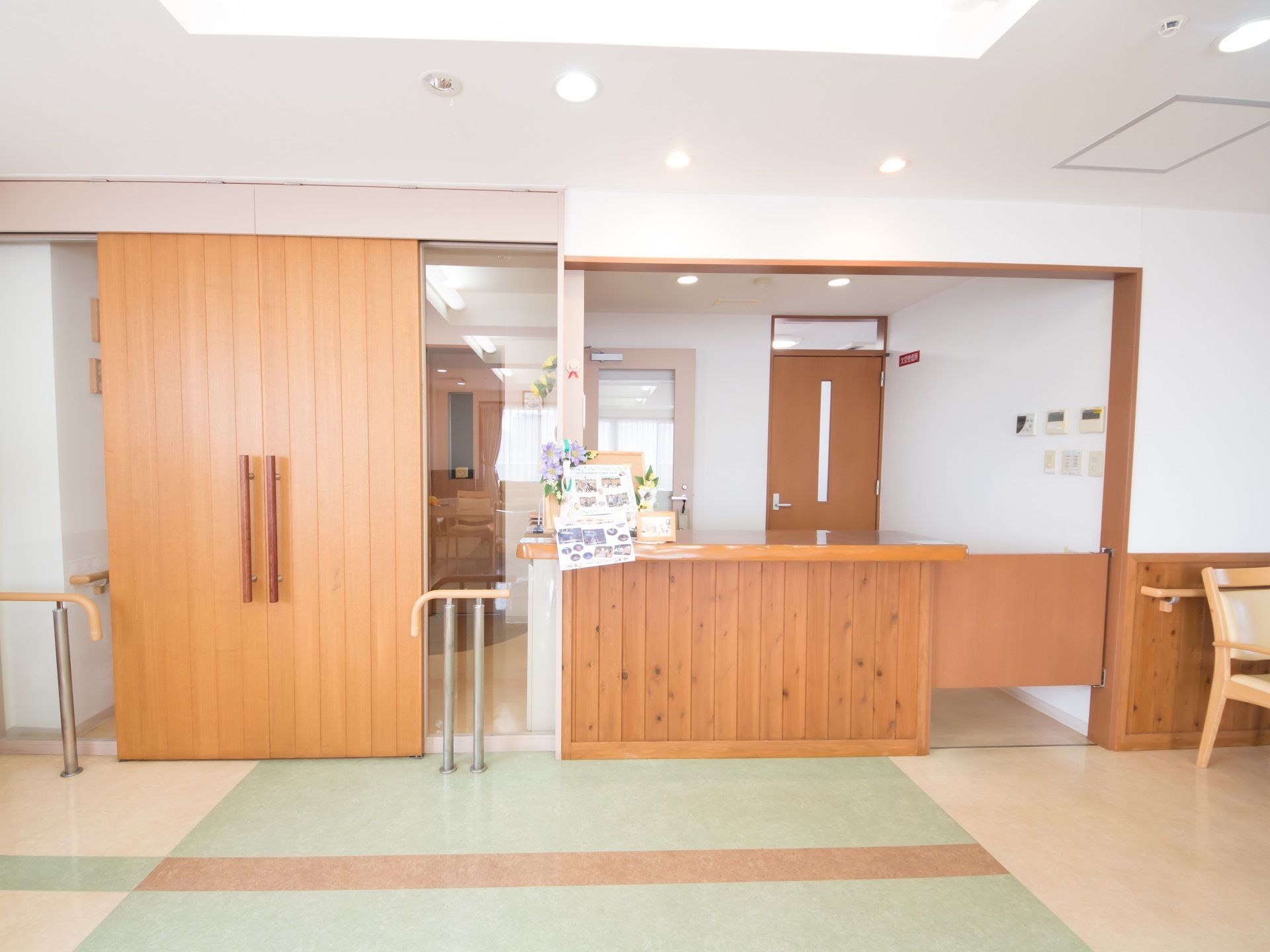 右側に受付カウンター、左側に出入口がある。出入口扉の両側には手すりが設置され、安全に配慮されている。