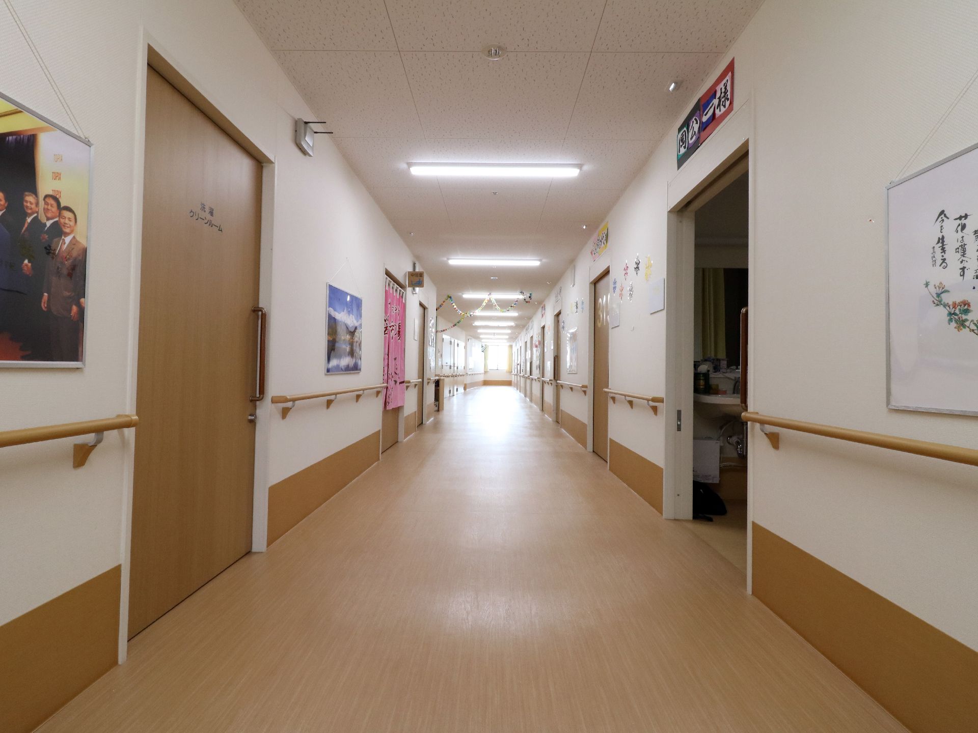 廊下の左右には手すりが設置してあり各部屋へ通じるドアは木目調になっている。長い廊下の突き当たりから光が差し込んでいる。