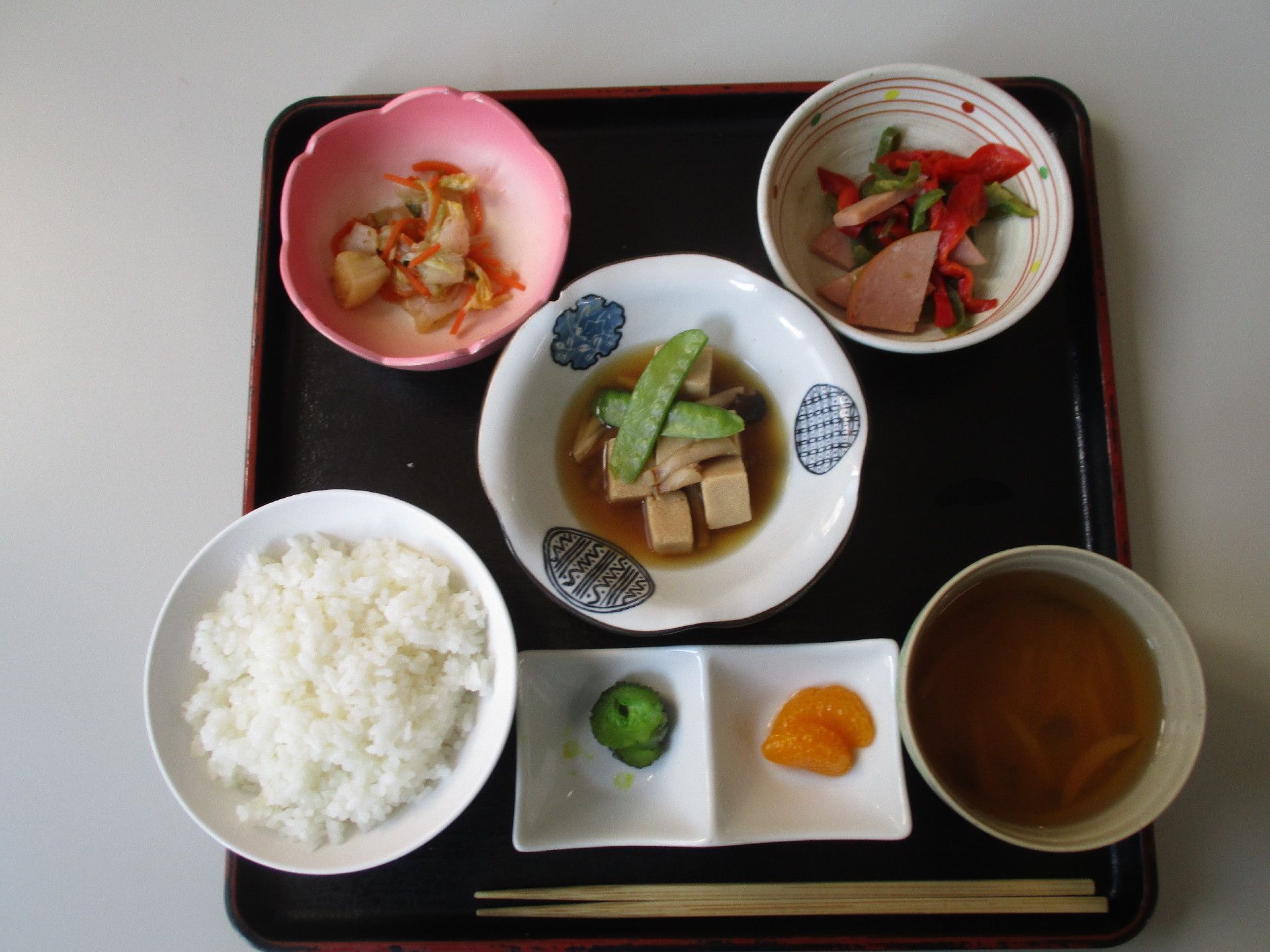 黒い四角いトレイに食事が用意されている。中央に絹さやののったメインに小鉢が2種と漬物、ご飯に味噌汁が提供されています。
