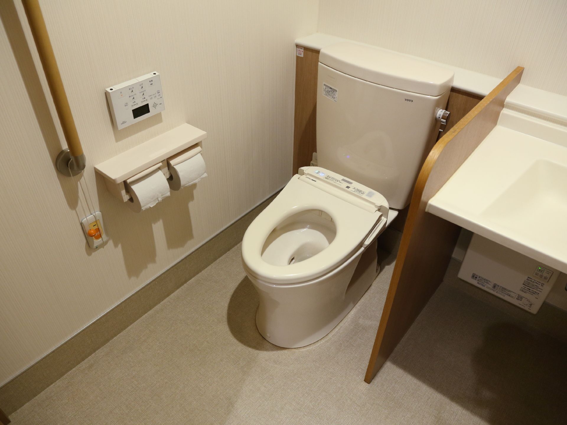 トイレは、温水洗浄機能付きである。壁には、手すりや呼び出しボタン取り付けられている。同じ空間に洗面台が設置されている。