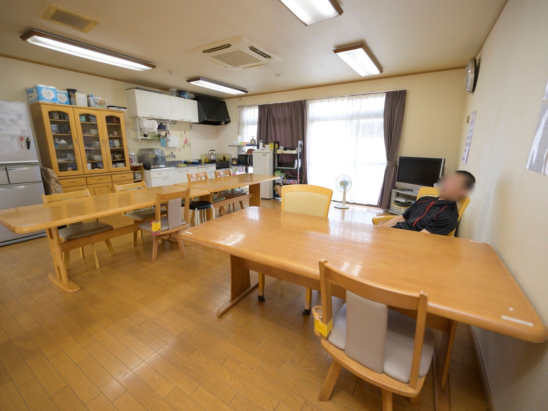 ダイニングテーブルが並べられたフローリングの食堂がある。壁際にはキッチンがあり、冷蔵庫や食器棚も置かれている。