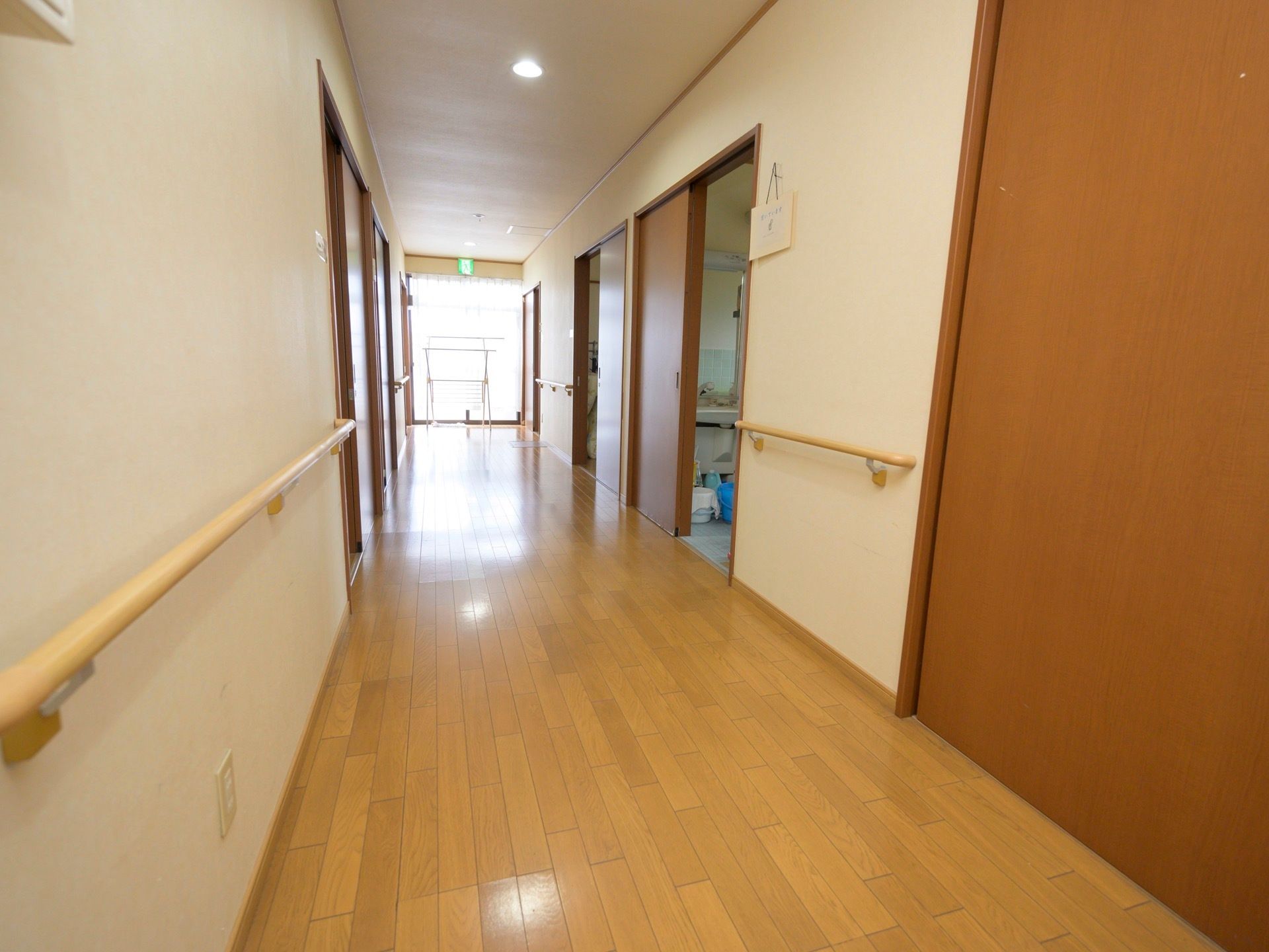フローリングが敷かれた廊下が続いている。壁には手すりが設置されており、突き当たりには採光窓が設けられている。