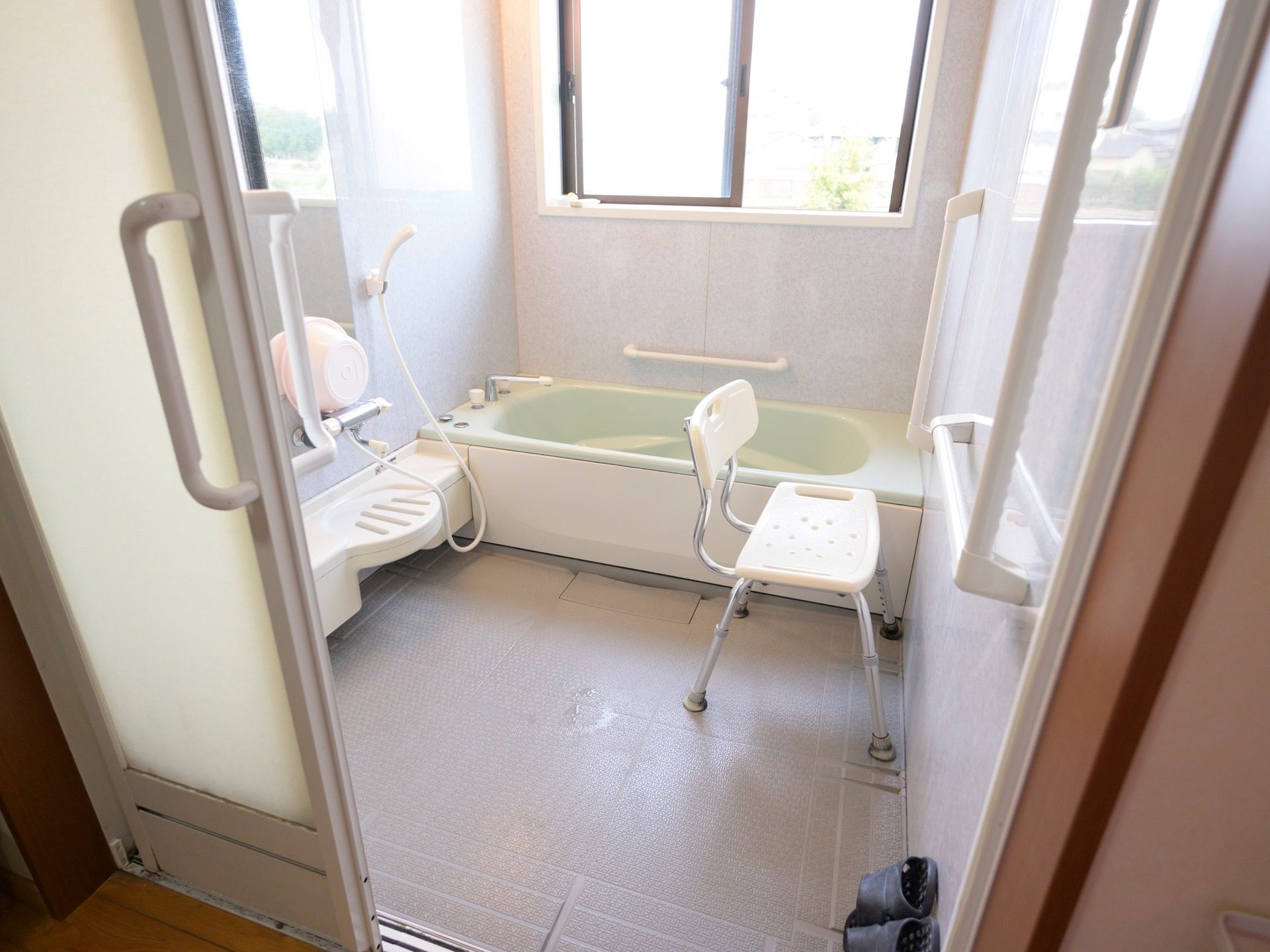 引き戸で仕切られた明るい浴室がある。白いシャワー椅子が置かれ、周りの壁には手すりがある。