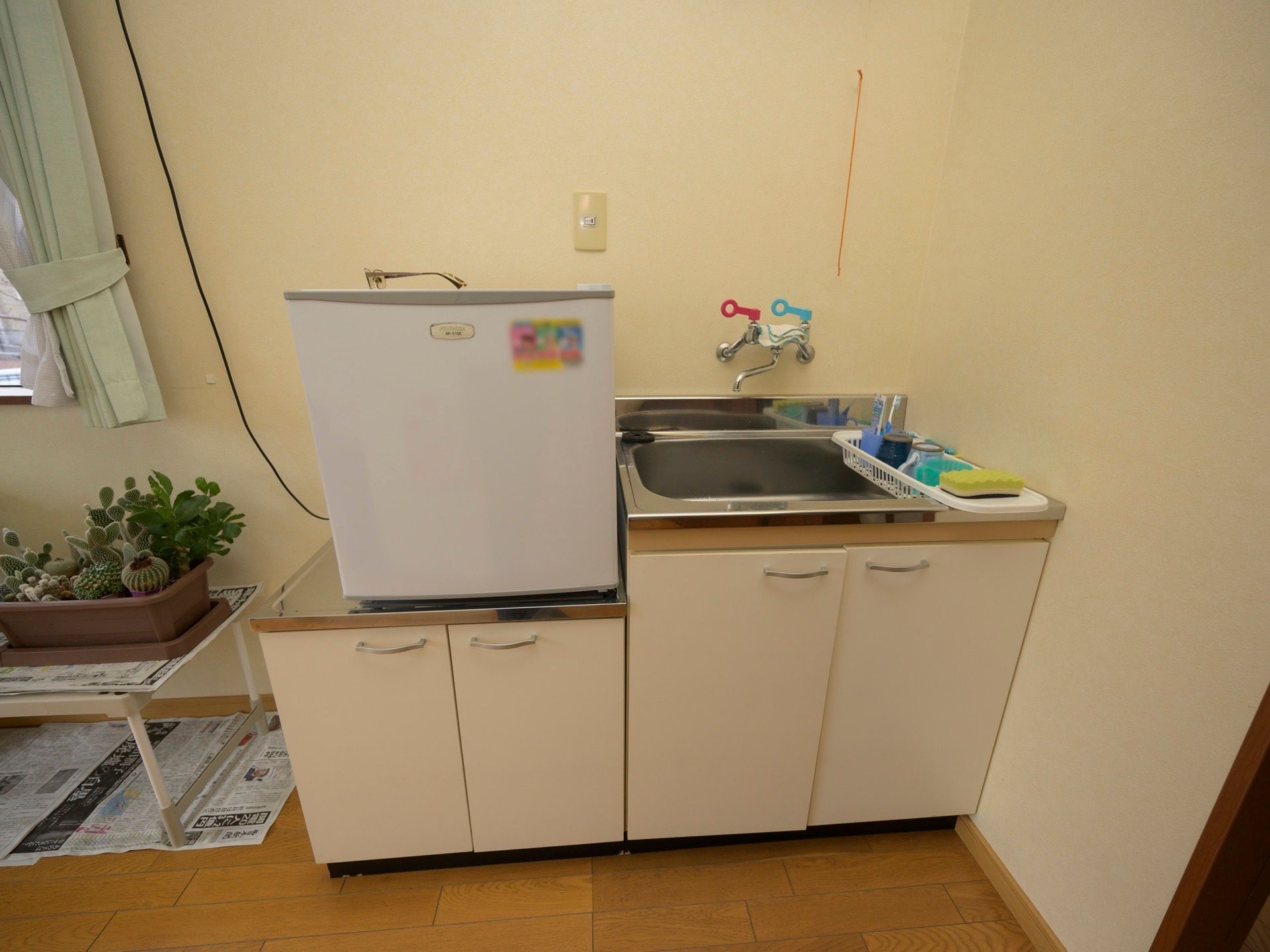 収納棚の付いた流し台が設置されている。台の上には小型の冷蔵庫が置かれており、シンク横にはスポンジなどがある。