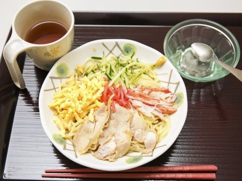 四角いお膳に乗っている食事は冷やし中華である。錦糸卵や蟹身、蒸し鶏などがのっており、お茶とお箸がある。