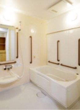 浴室の壁や浴槽はきれいに磨かれており、照明の光が明るく反射している。浴室内には洗面台のほか、手すりやつかまり用の棒が設置されている。