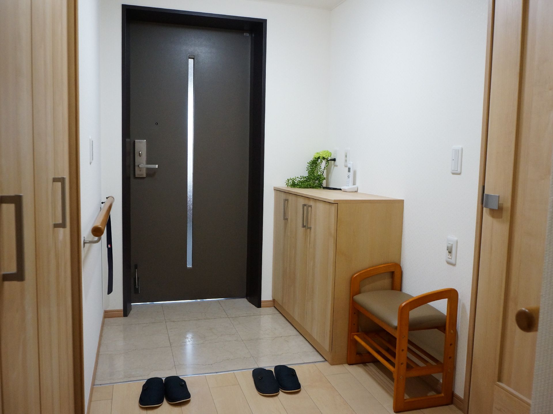 居室の玄関は、バリアフリー設計である。入って左手に下駄箱があり、横に椅子が置かれている。反対の壁に、手すりがついている。