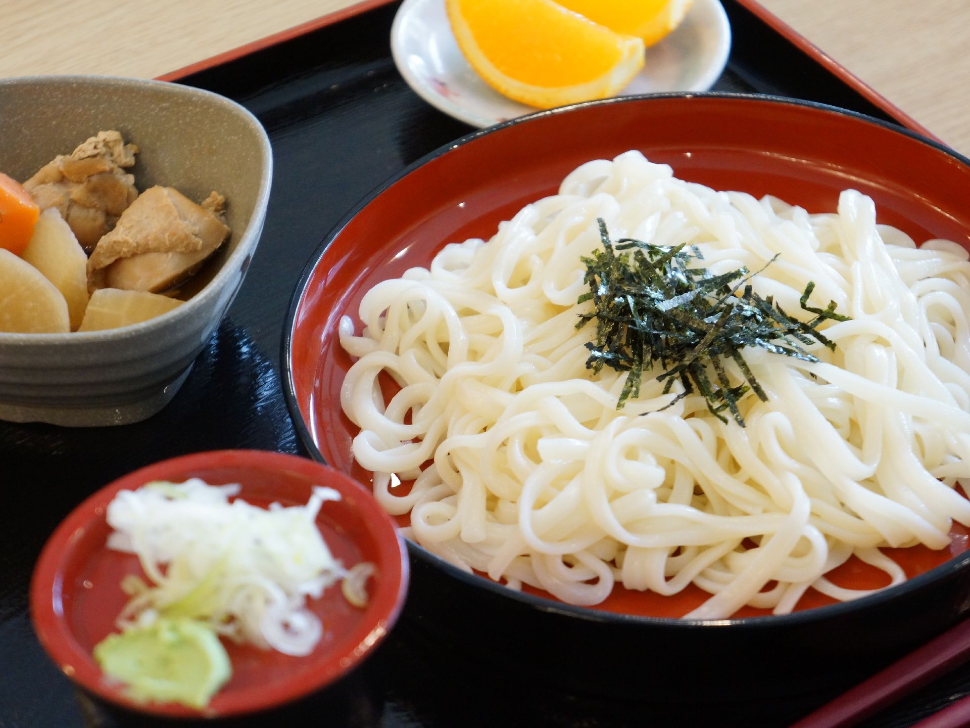 冷やしうどんに、煮物、フルーツが添えられている食事