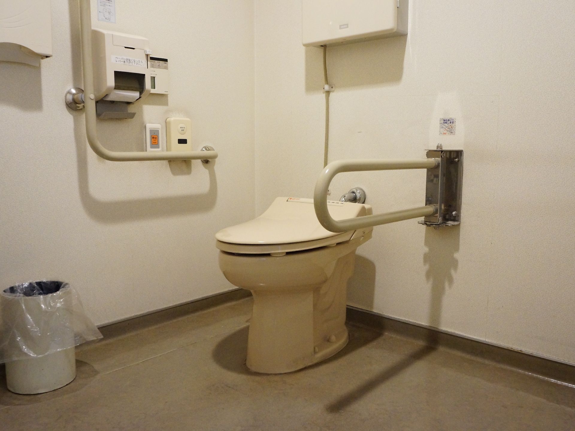 洋式トイレの両側に、手すりが取り付けられている。右側の壁に、トイレのスイッチとナースコールが設置されている。
