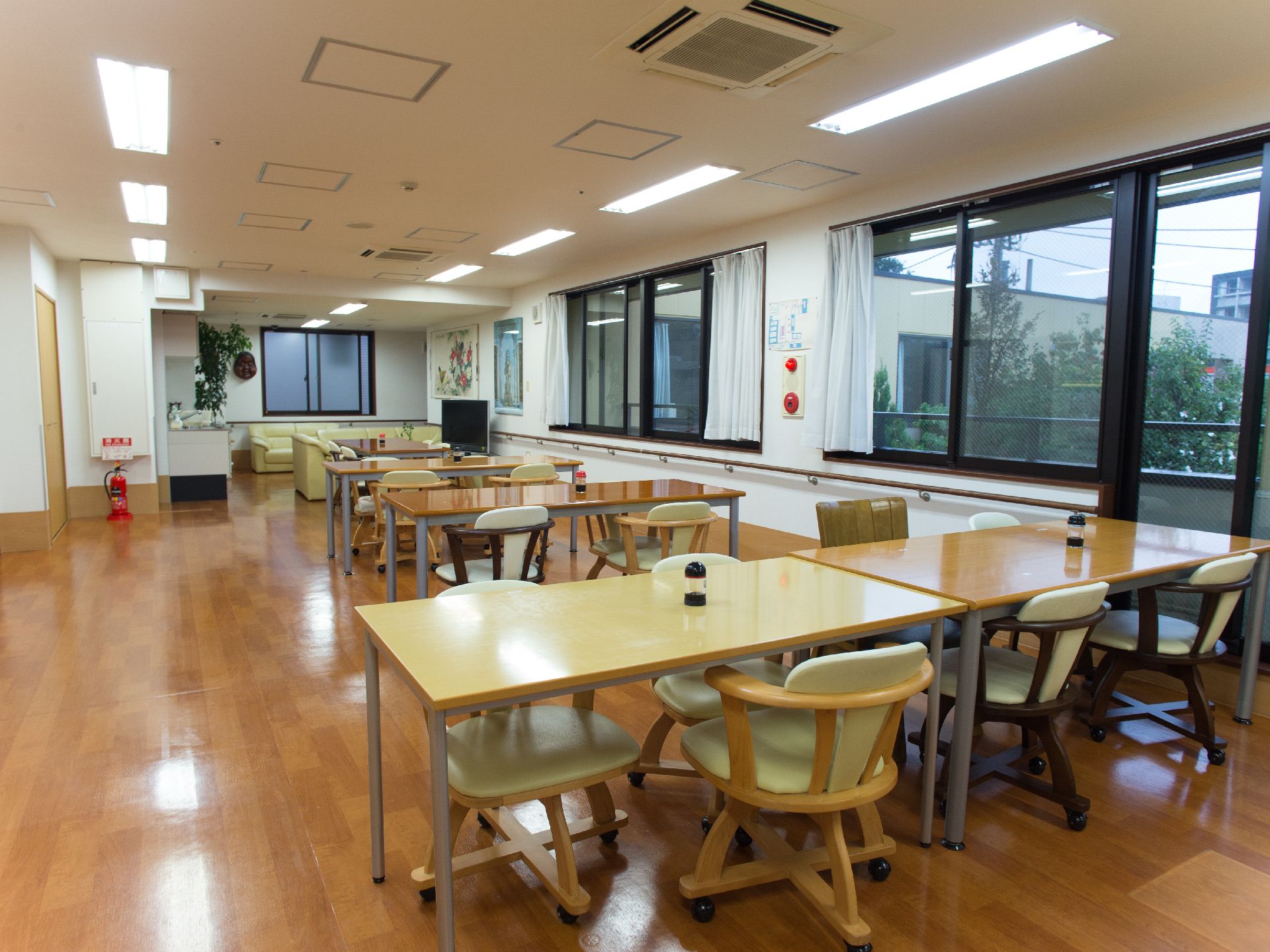 床はフローリングになっている。右側には窓が2つある。多くのテーブルと椅子がある。テーブルの上には醤油が置いてある。