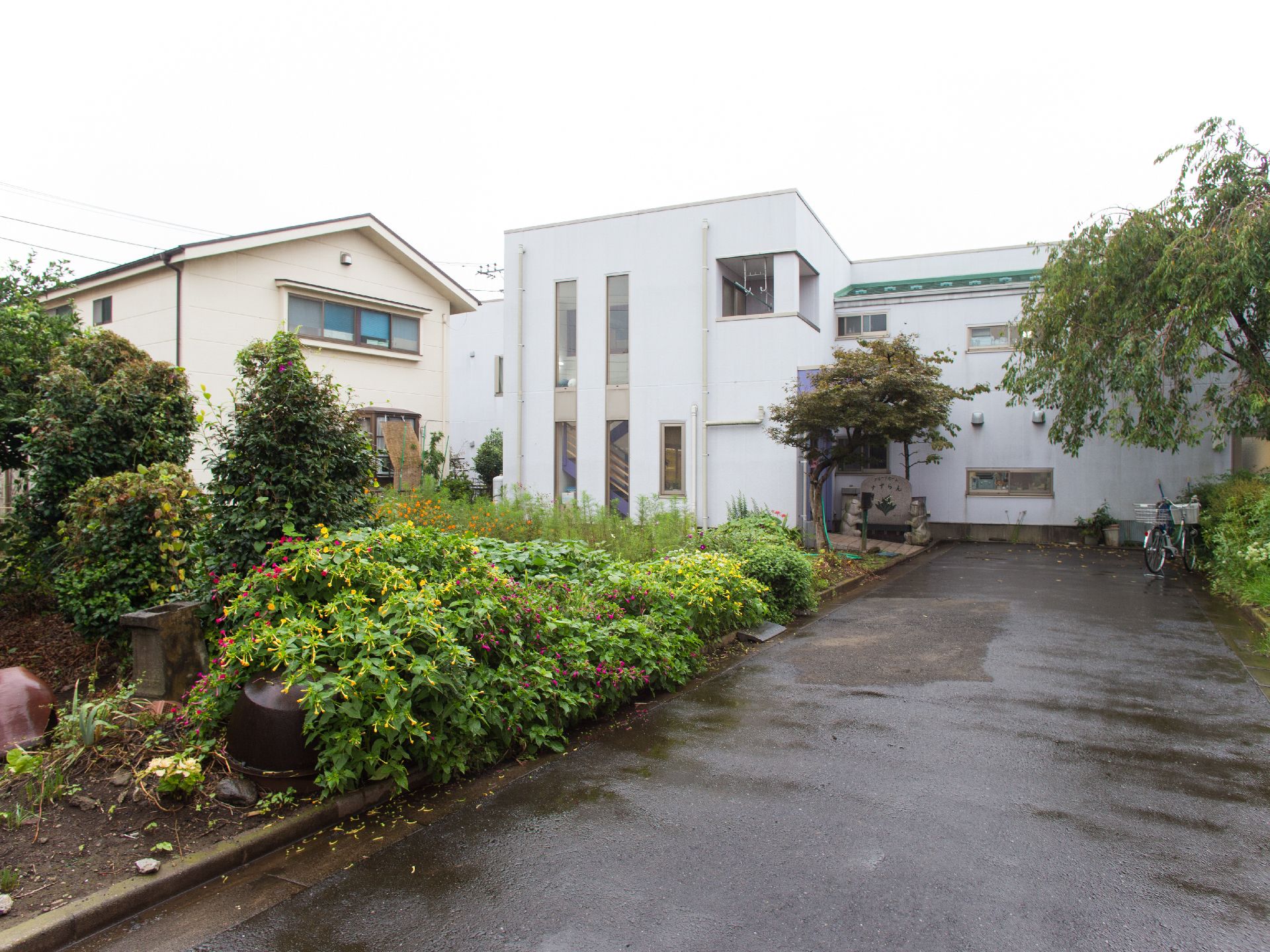 左側には自家菜園がある。奥には建物がある。建物の右側には表札がある。道をまっすぐ進むと行き止まりになる。