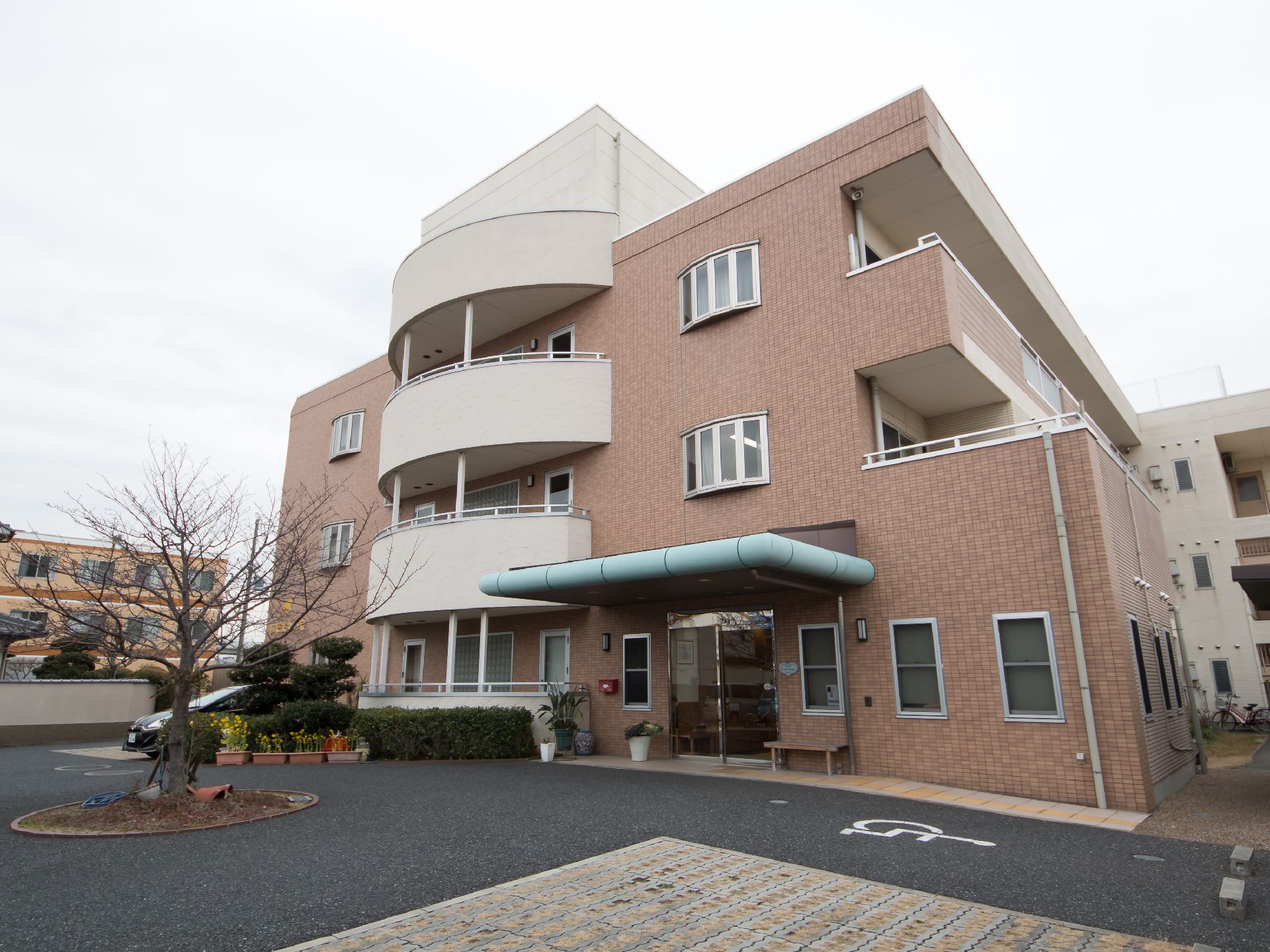レンガ調の壁の三階建ての大きな建物。半円形のバルコニーがついている。大きなルーフのついた自動ドアの玄関がある。
