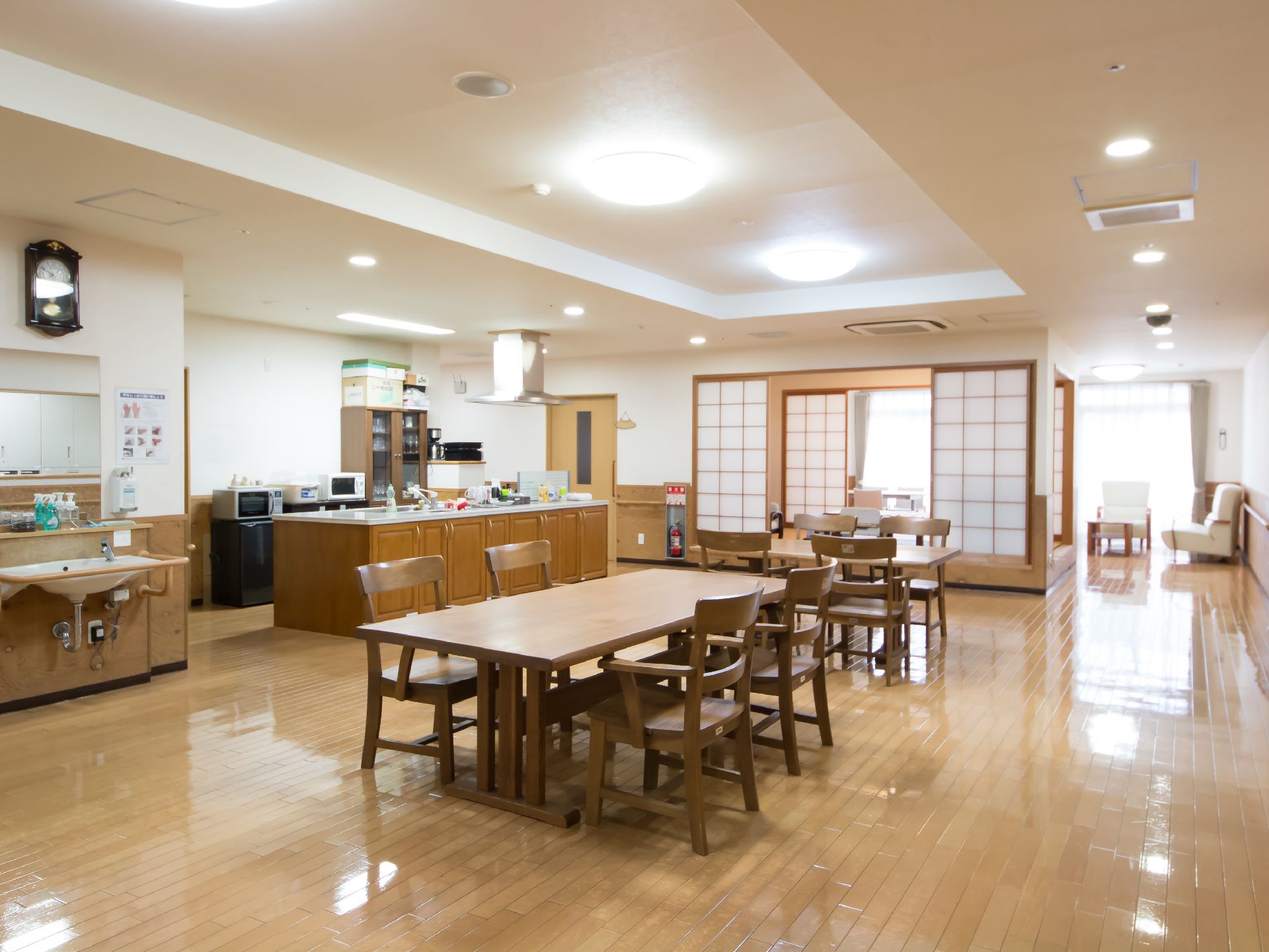 広い食堂にテーブルと椅子がたくさん並んでいる。奥には障子で囲まれた和室のスペースがある。キッチンカウンターと洗面台が設けられている。