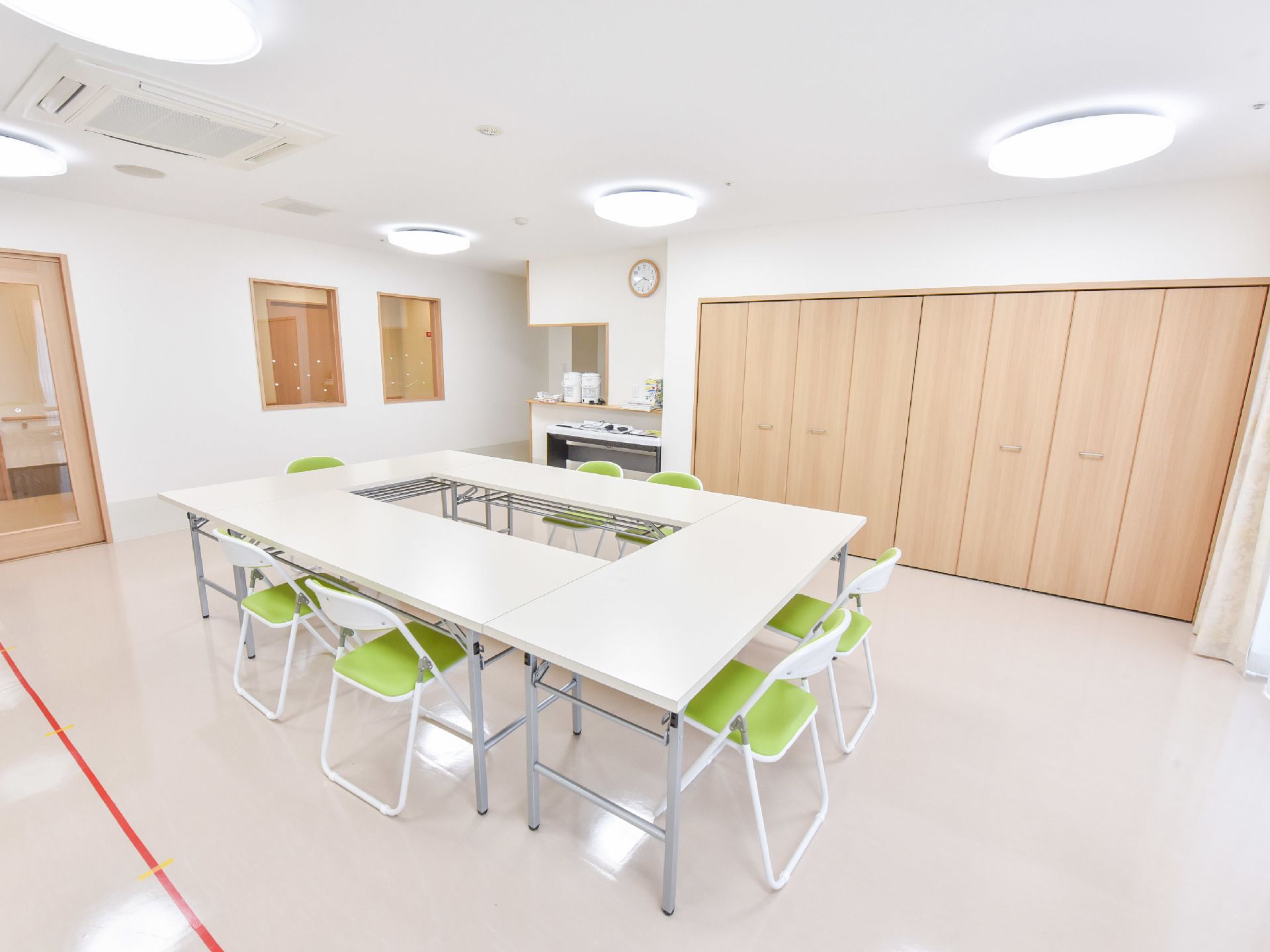 地域交流室には白い長テーブルと椅子が置かれている。ドアはガラス状で外から中が分かるようになっている。窓も2つある。