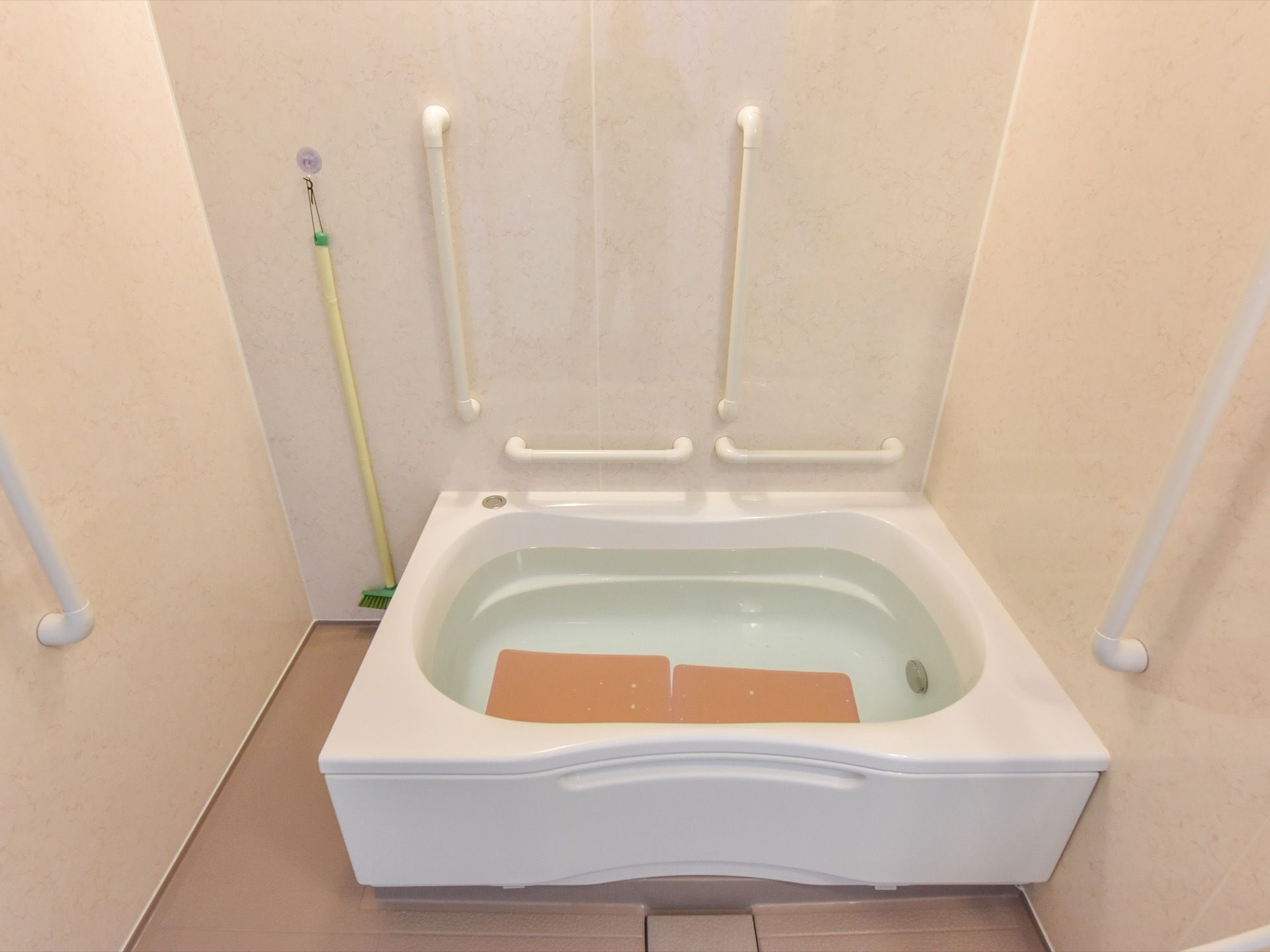 浴室には複数の手すりが設置されている。浴槽内には、足を滑りにくくするマットを配置している。壁に掃除用具がかかっている。