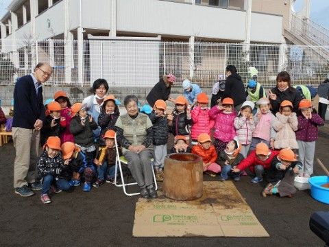 庭で椅子に腰掛ける入居者様を囲む、園児たちやスタッフ
