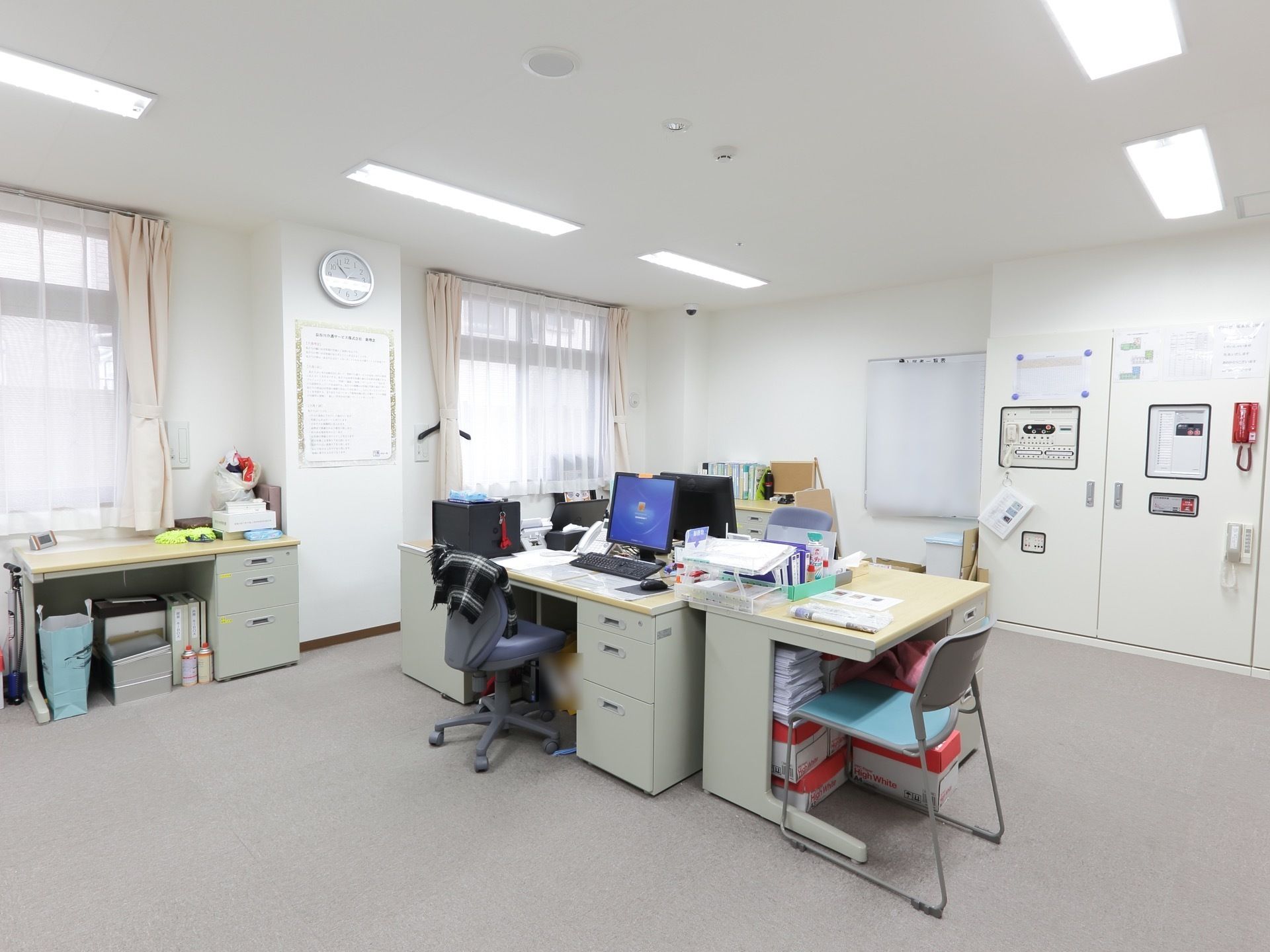 スタッフルームは、白を基調とした明るい部屋である。壁には白いスケジュールボードが２つ貼られている。時計も掛けられている。