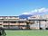 屋上の床や壁は緑色に塗られており、その上にはフェンスが建てられている。街並みの向こうには山が見え、うっすらと雪がかかっている。